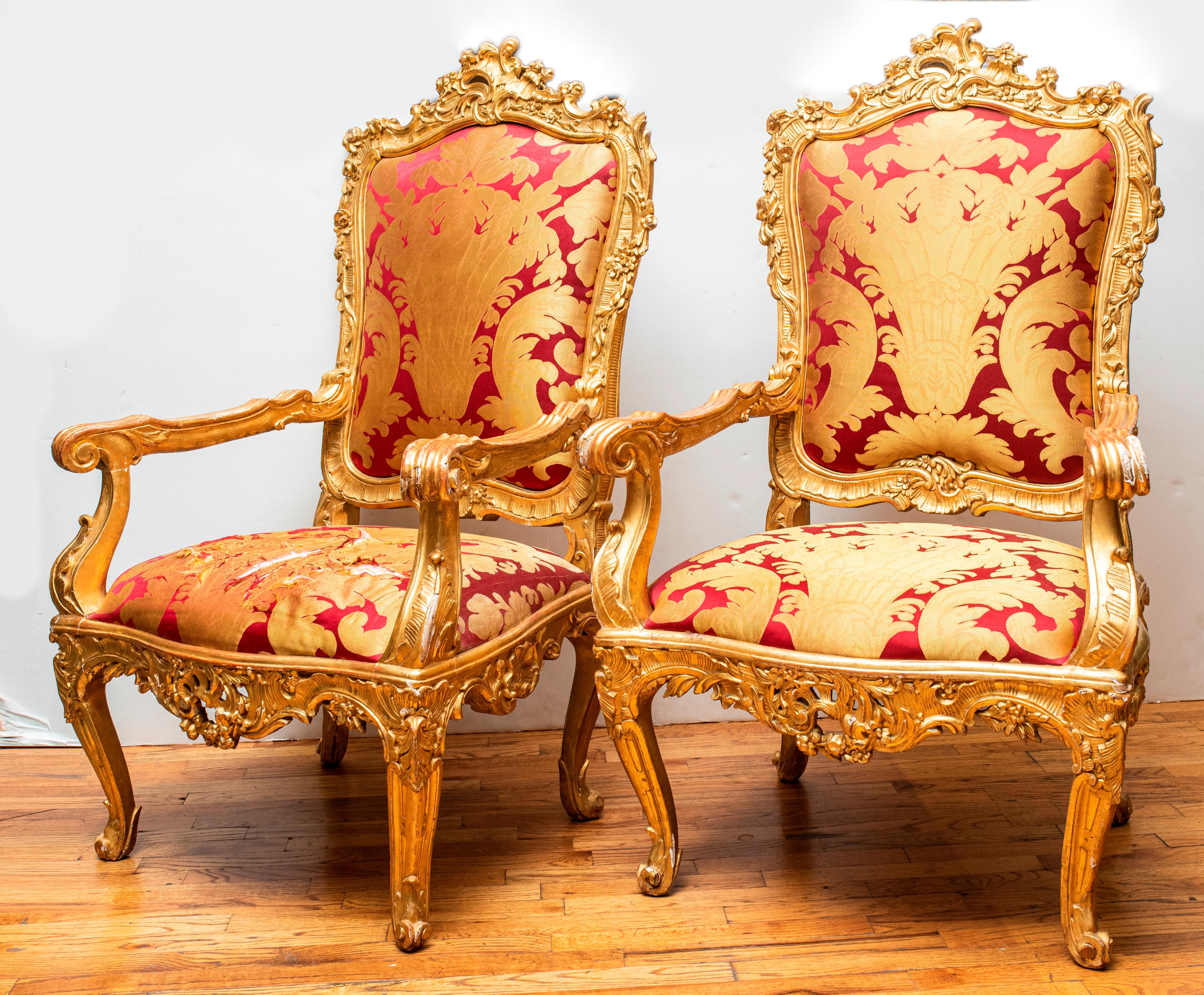 Italian Rococo period pair of ornate carved giltwood throne armchairs with upholstery, mid-18th century. Tears to seat upholstery on one chair. Measures: 52.5