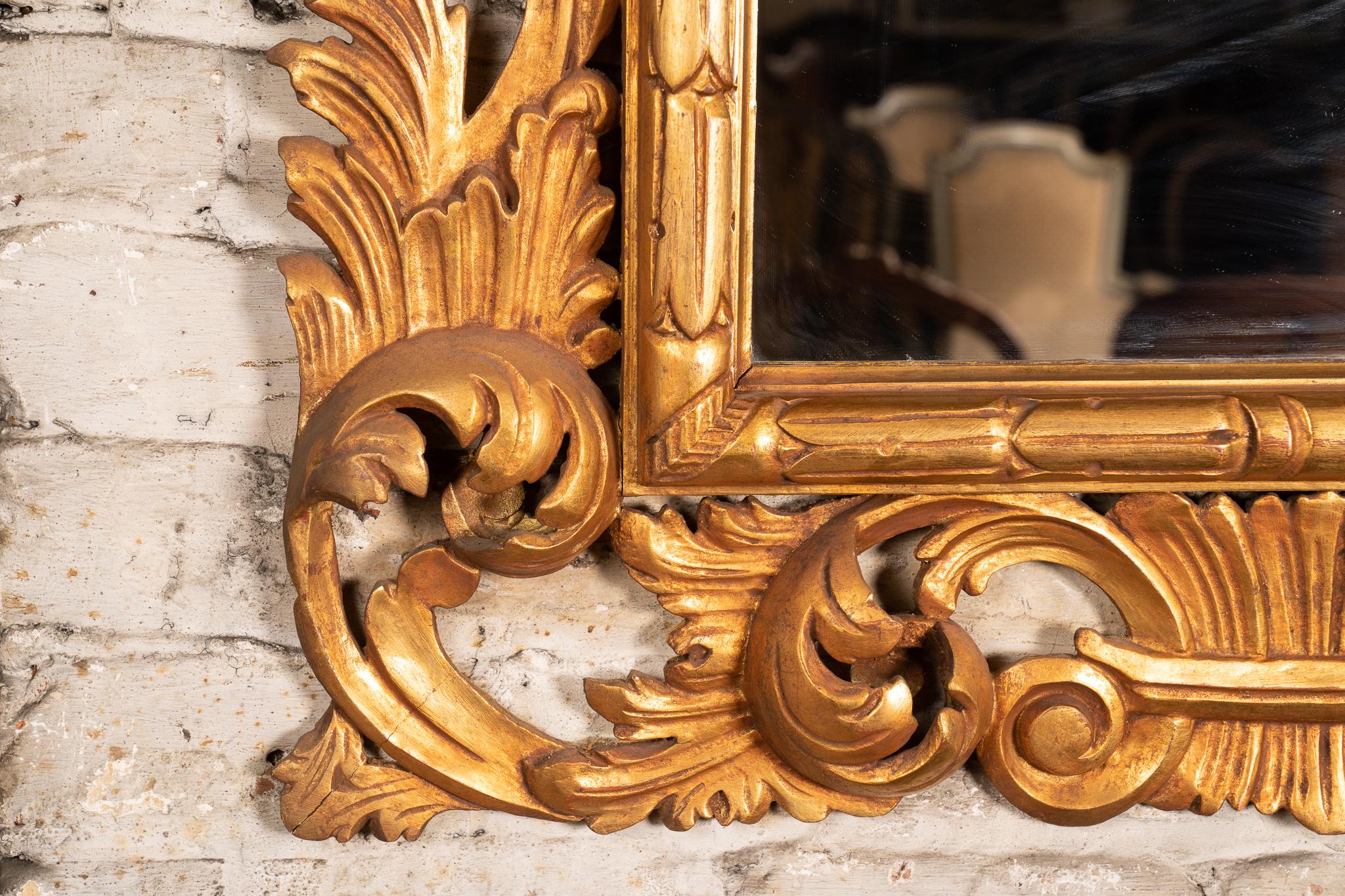 This Italian Roccoco style mirror features ornate, heavy carvings and is painted with gold leaf throughout. The 20th century gilt wood mirror has a simply patterned inner frame, which is surrounded by scrolling acanthus leaves mirroring the shape of