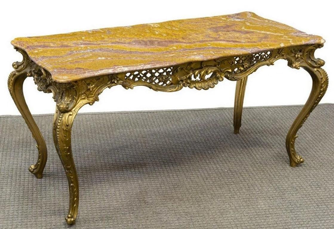 Une table basse spectaculaire, faite sur mesure, de style rococo italien Louis XV. Le plateau en onyx rouge et orange surmonte le tablier en bois doré sculpté à la main, très décoratif, avec des motifs ajourés, enroulés et feuillus. Les sculptures