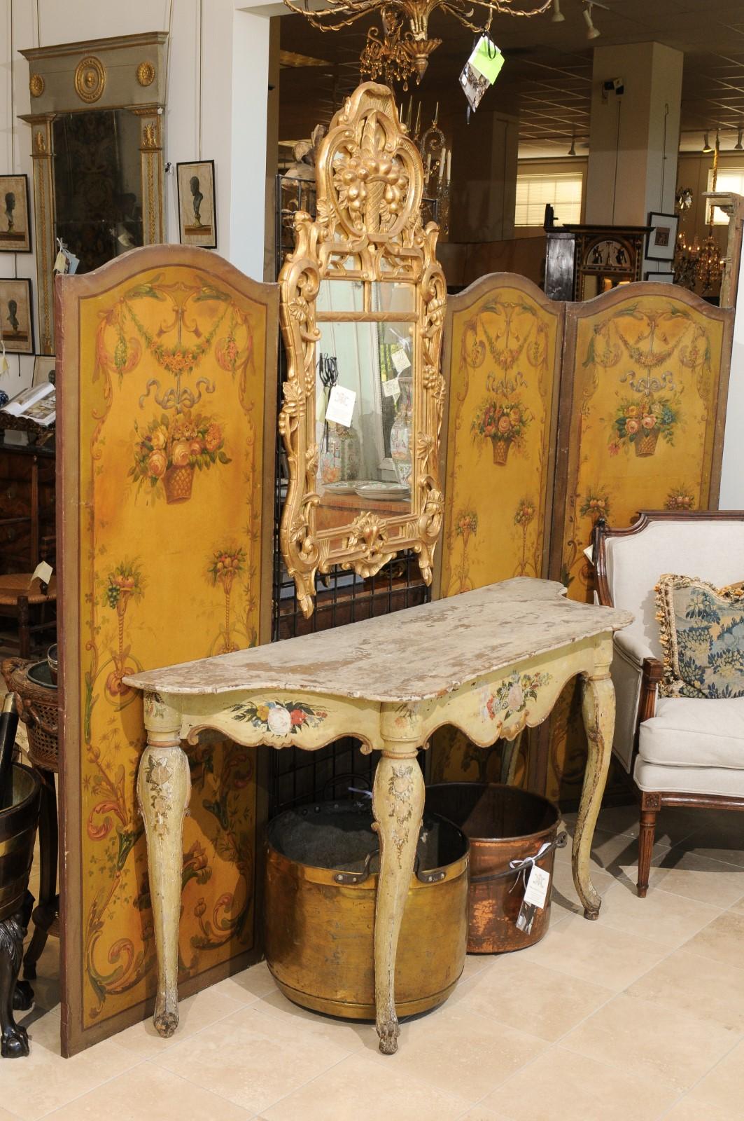 A mid-18th century Italian Rococo console table in a pale yellow painted finish with serpentine sided top, floral decoration on shaped apron and cabriole legs ending in hoofed feet.
