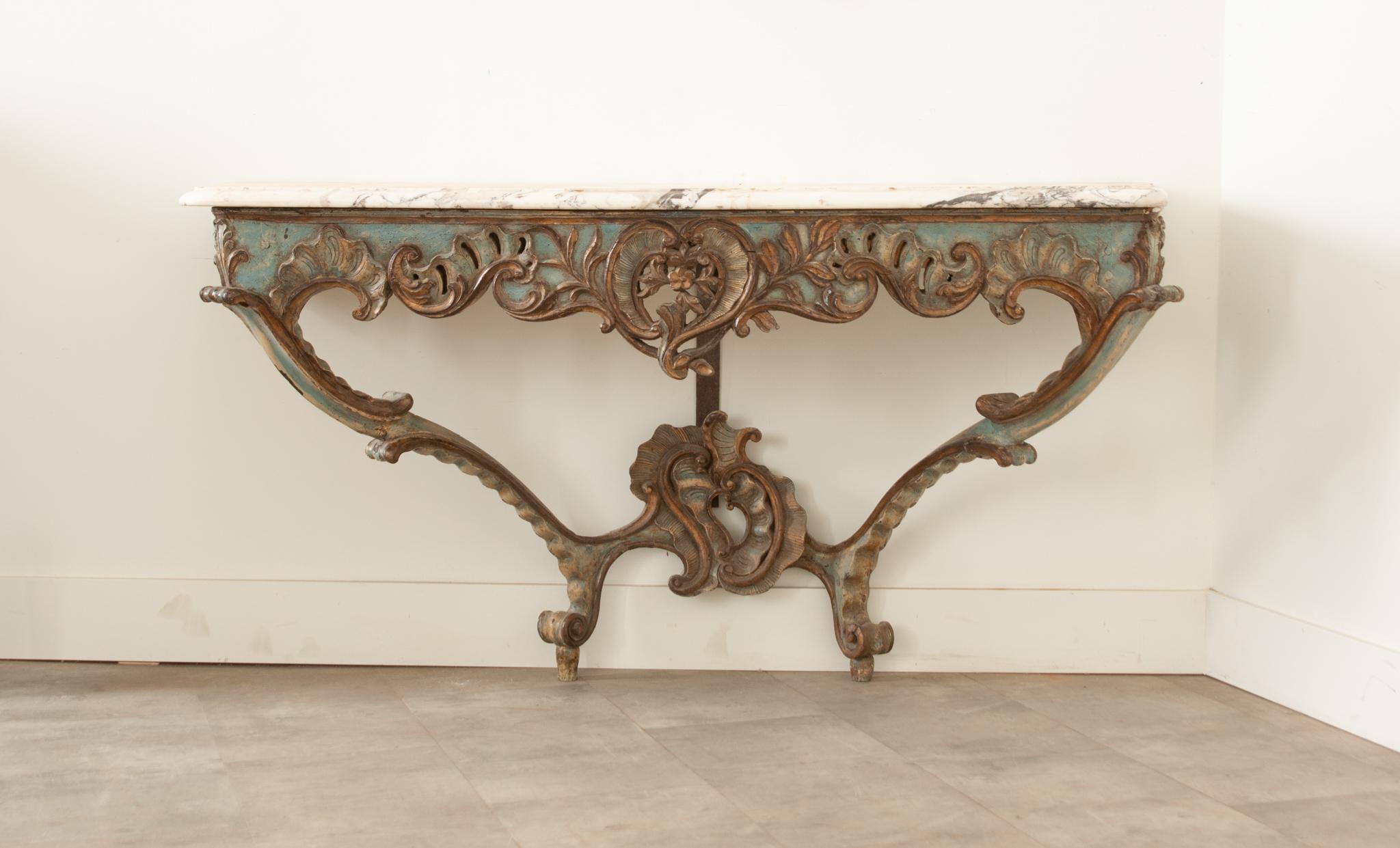 A gorgeous Rococo console table with original serpentine marble top over a pierced apron. Asymmetrical in design, featuring deeply carved C & S scrolls throughout. The table must be connected flat to the wall with added support from an iron bar. The