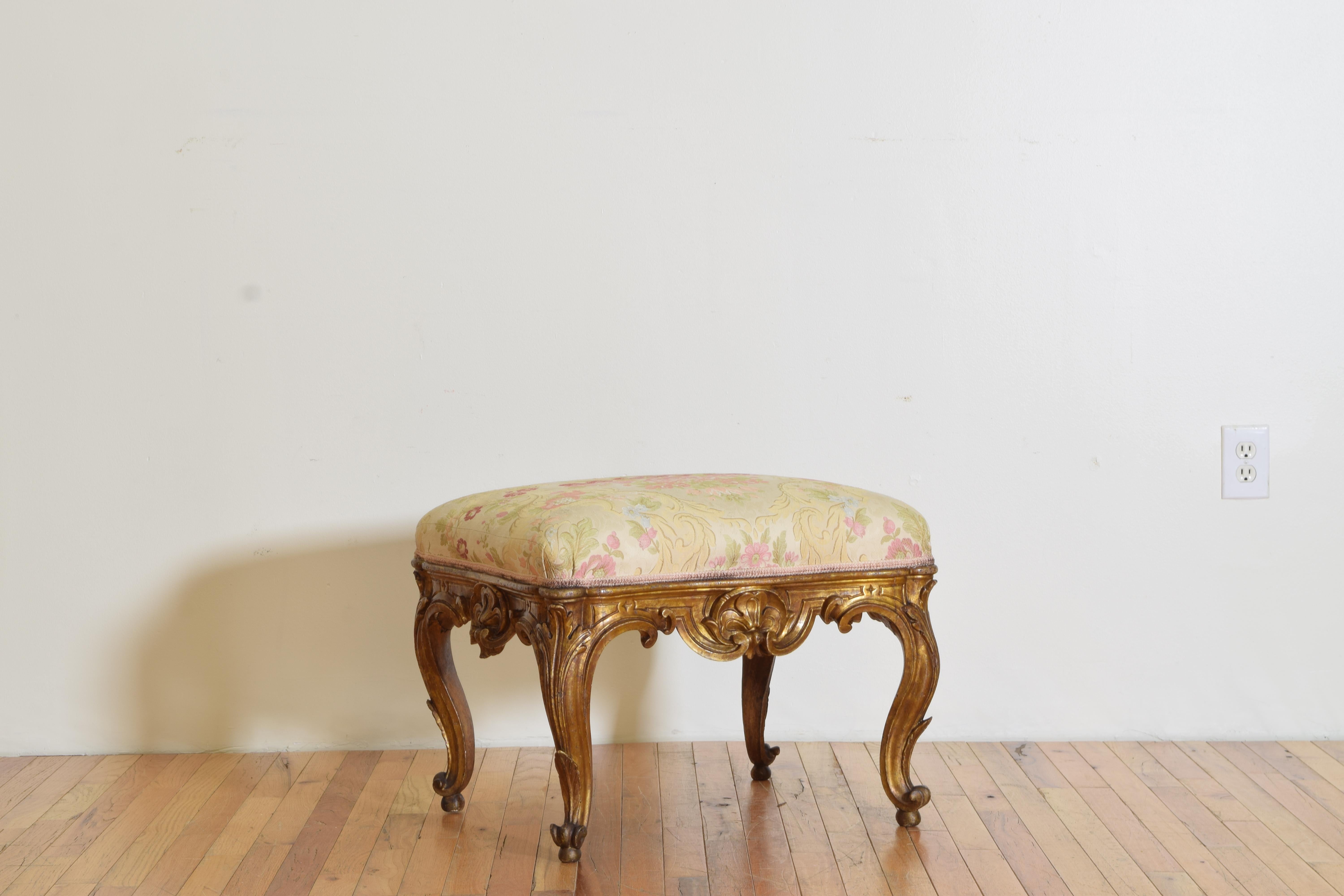 Having an upholstered seat above a carved giltwood frame with shell and scroll motifs, the cabriole legs terminating is split toe feet.