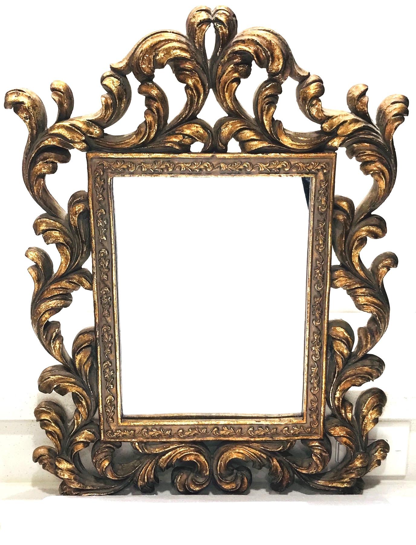 Hollywood Regency Baroque style mirror features a solid wood frame with hand carved designs and antique gold leaf finish. The ornamental frame features stylized scrolls of foliage and Prince of Wales plumes. The rectangular inner frame has a series