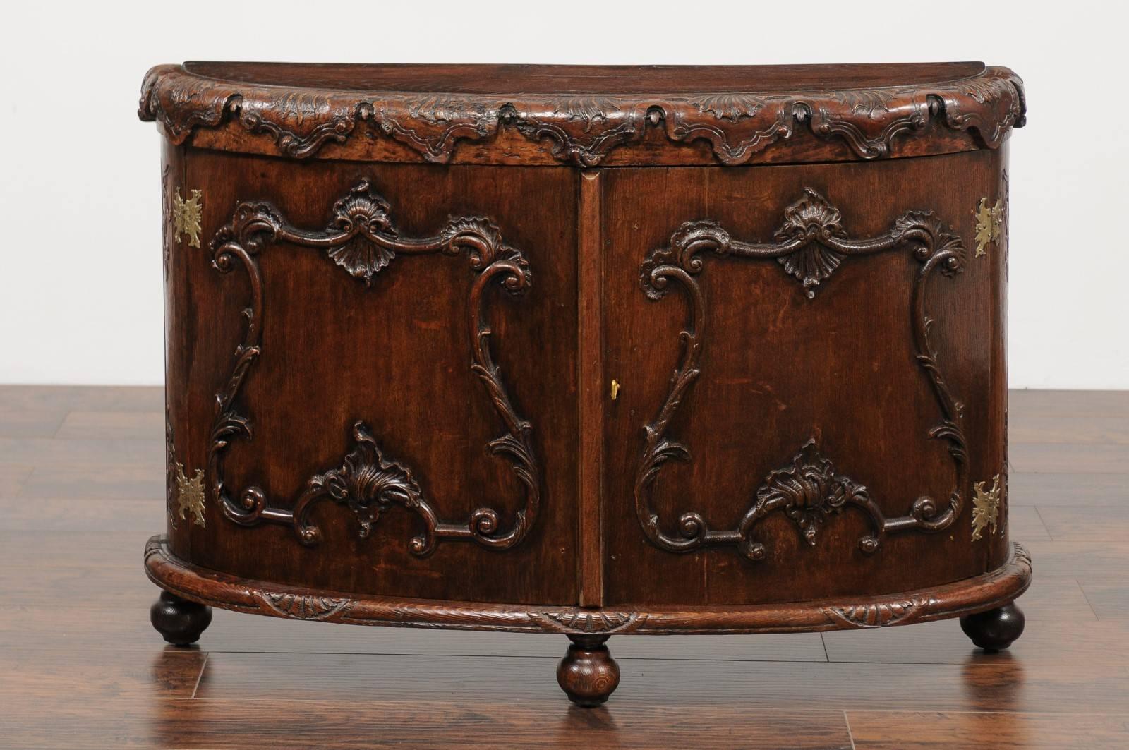 An Italian Rococo style hand-carved oak two-door demilune cabinet with cartouche motifs from the early 19th century. This Italian credenza features an exquisite semi-circular top, adorned in the front with carved foliage motifs. The demi-lune façade