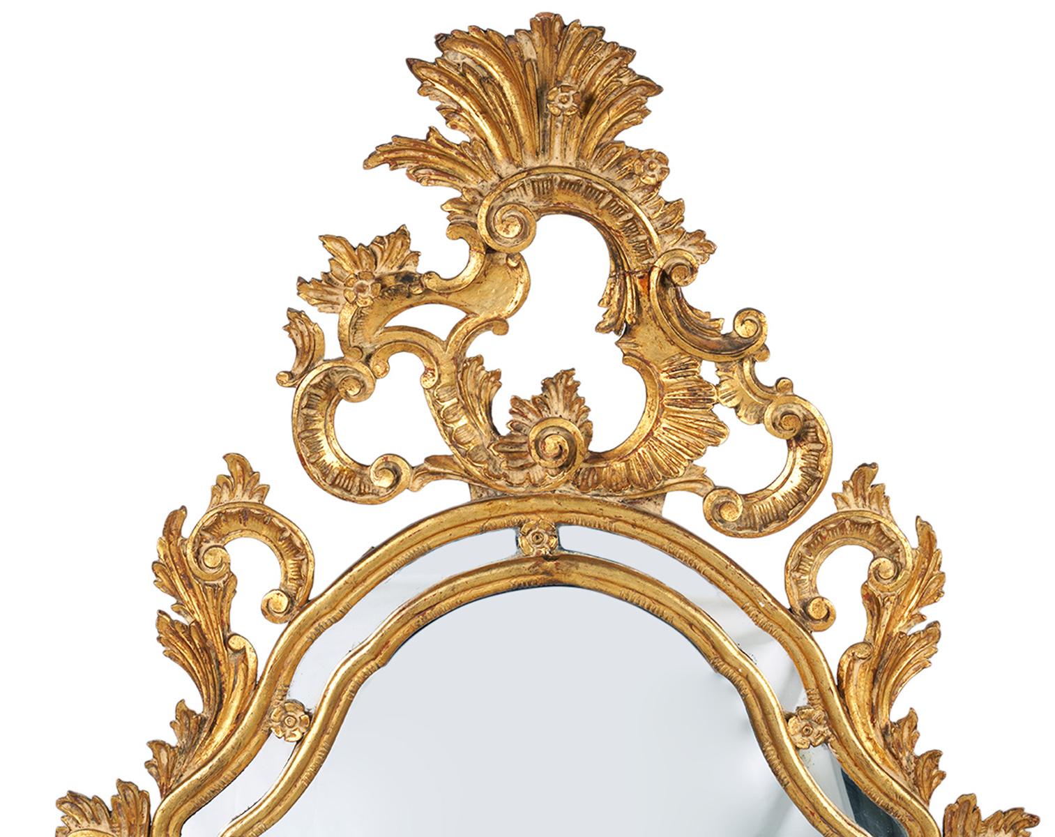 Grandiosely fashioned and carved in the rococo style this giltwood mirror features a plethora of scrolls and leaf work surmonted by a sunburst style crest. The main mirror is surrounded by shaped mirrored panels creating an elegant and lightfilled