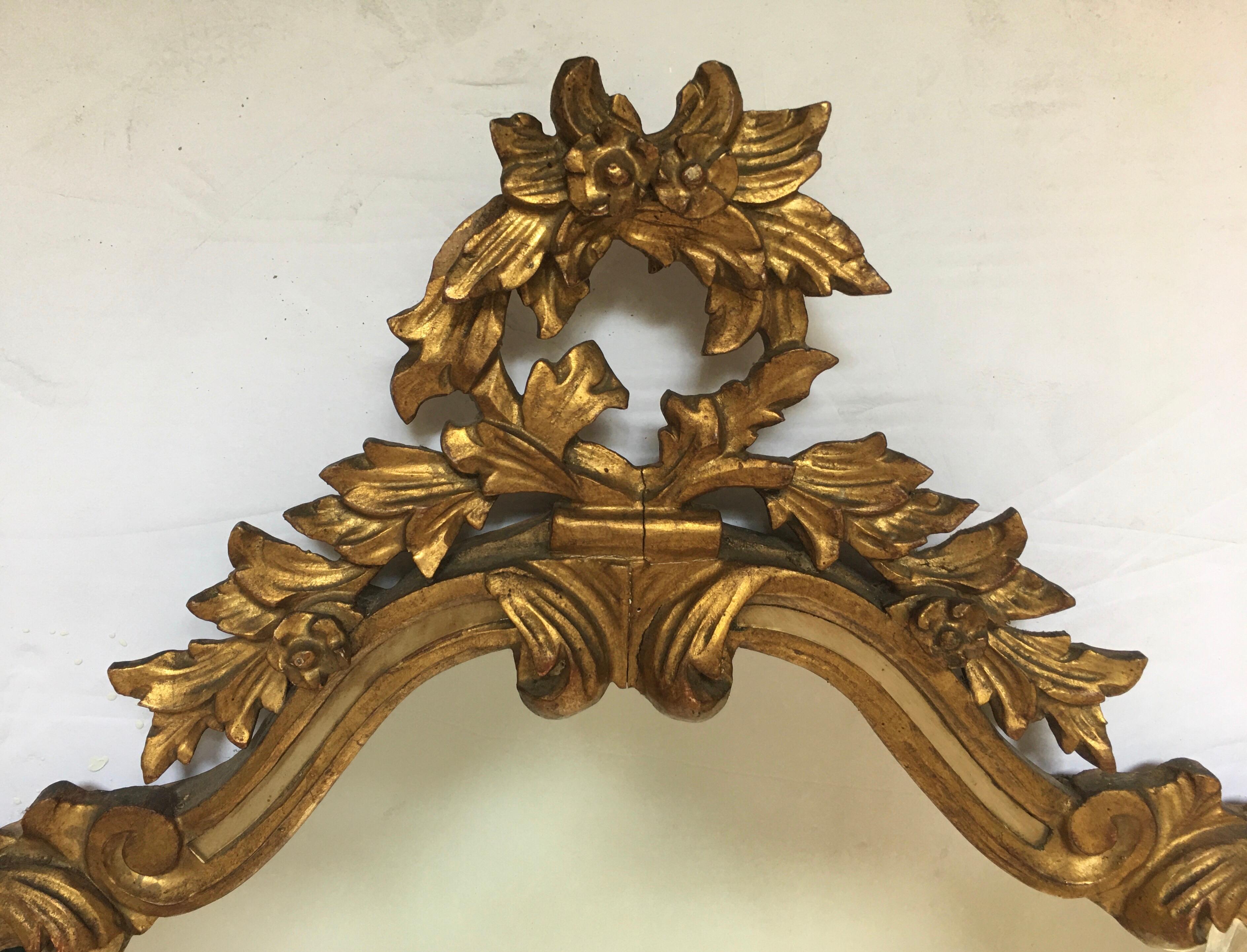 Italian Rococo style carved giltwood wall mirror with floral and acanthus leaf details. This Hollywood Regency style mirror is trimmed in aged mirror. Paper label 'Made In Italy' and branded to Verso 'Made in Italy'.