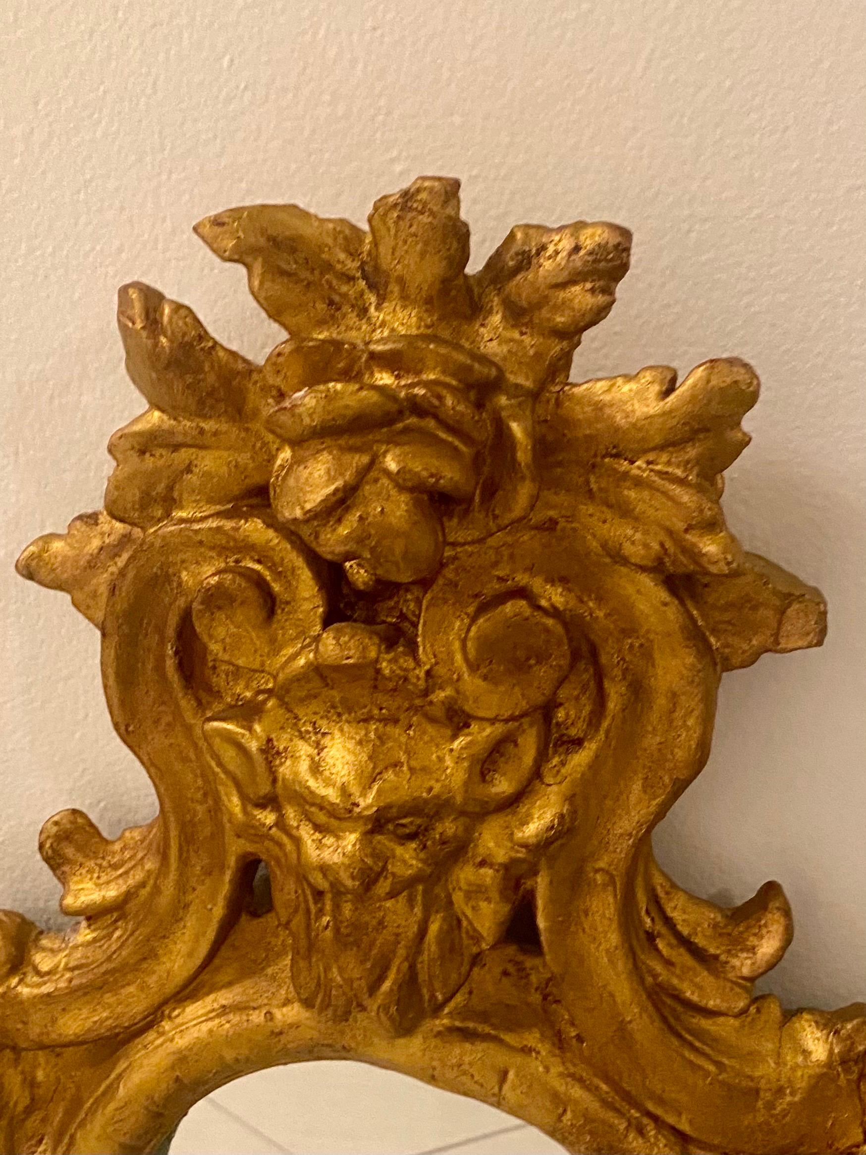Cet exceptionnel miroir ancien de style rococo en bois sculpté et doré est orné d'un cadre et de motifs floraux ainsi que d'un visage de fée de la forêt malicieux. 
