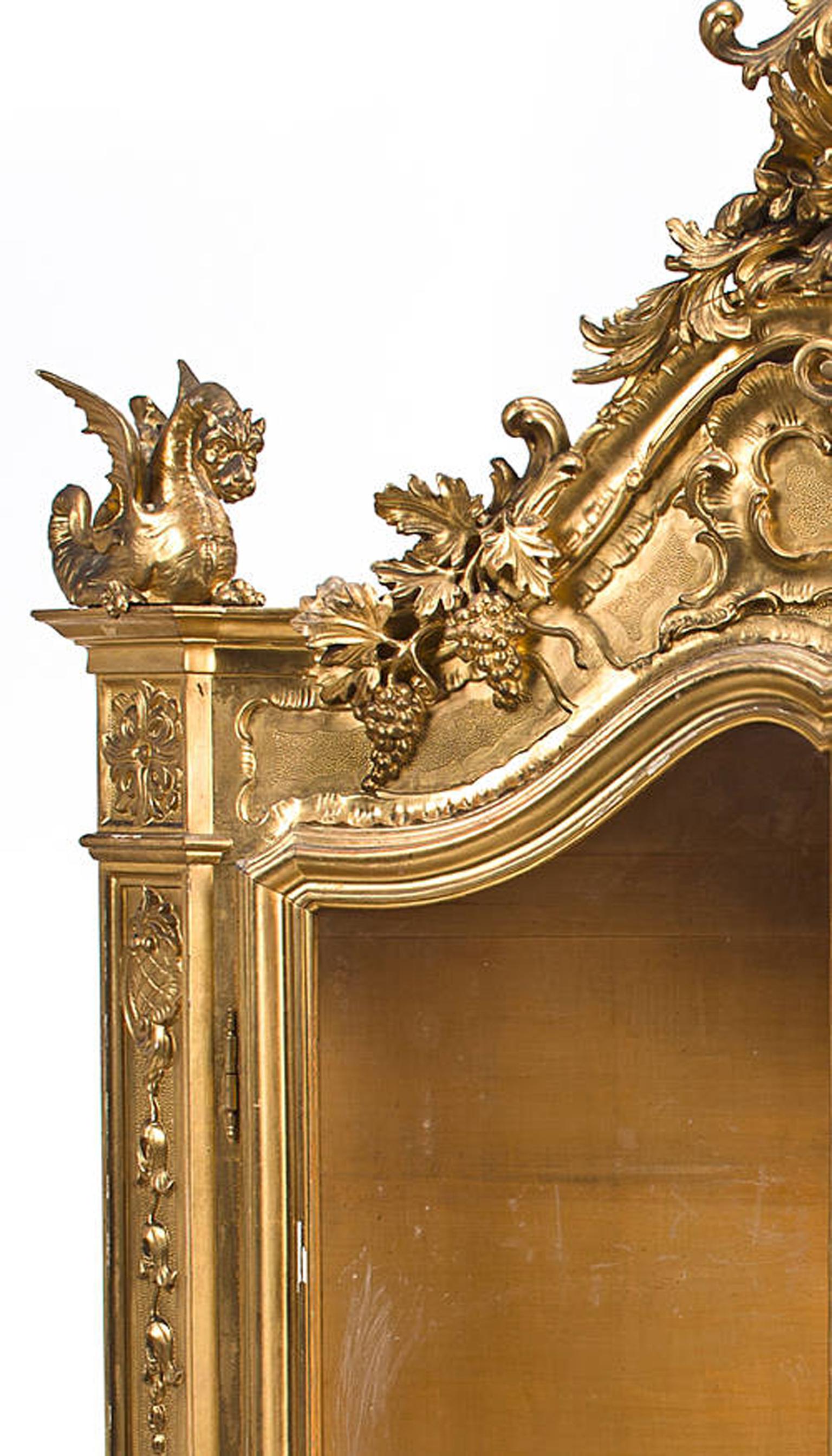 Impressive Venetian Rococo style giltwood vitrine cabinet, 19th century.
The finely carved giltwood vitrine is surmounted by a scrolling acanthus and floral bouquet, above a Rocaille shell motif pediment with grapes and winged dragons, over two