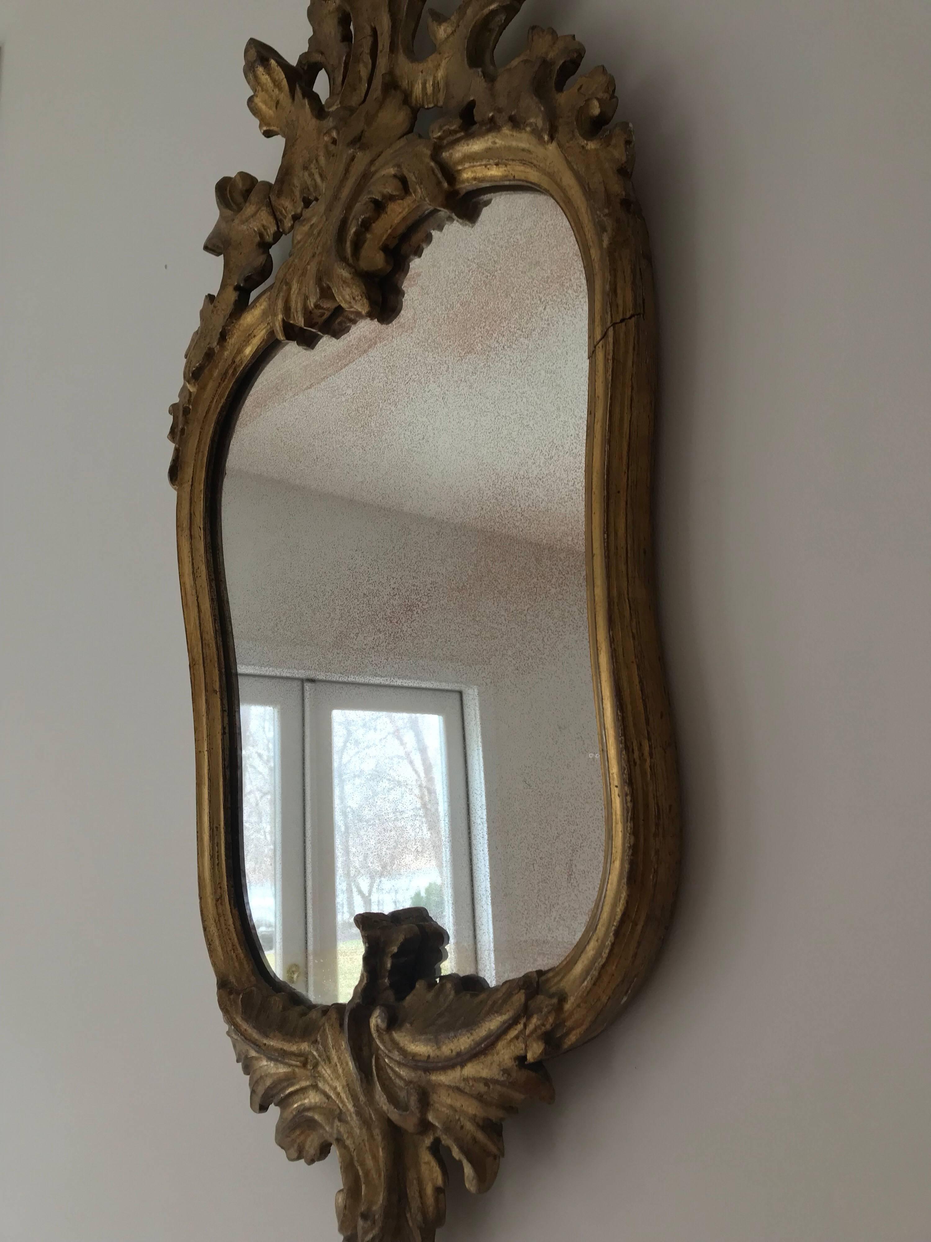 An early 20th century Italian Rococo style giltwood wall mirror. Antiqued mirror.