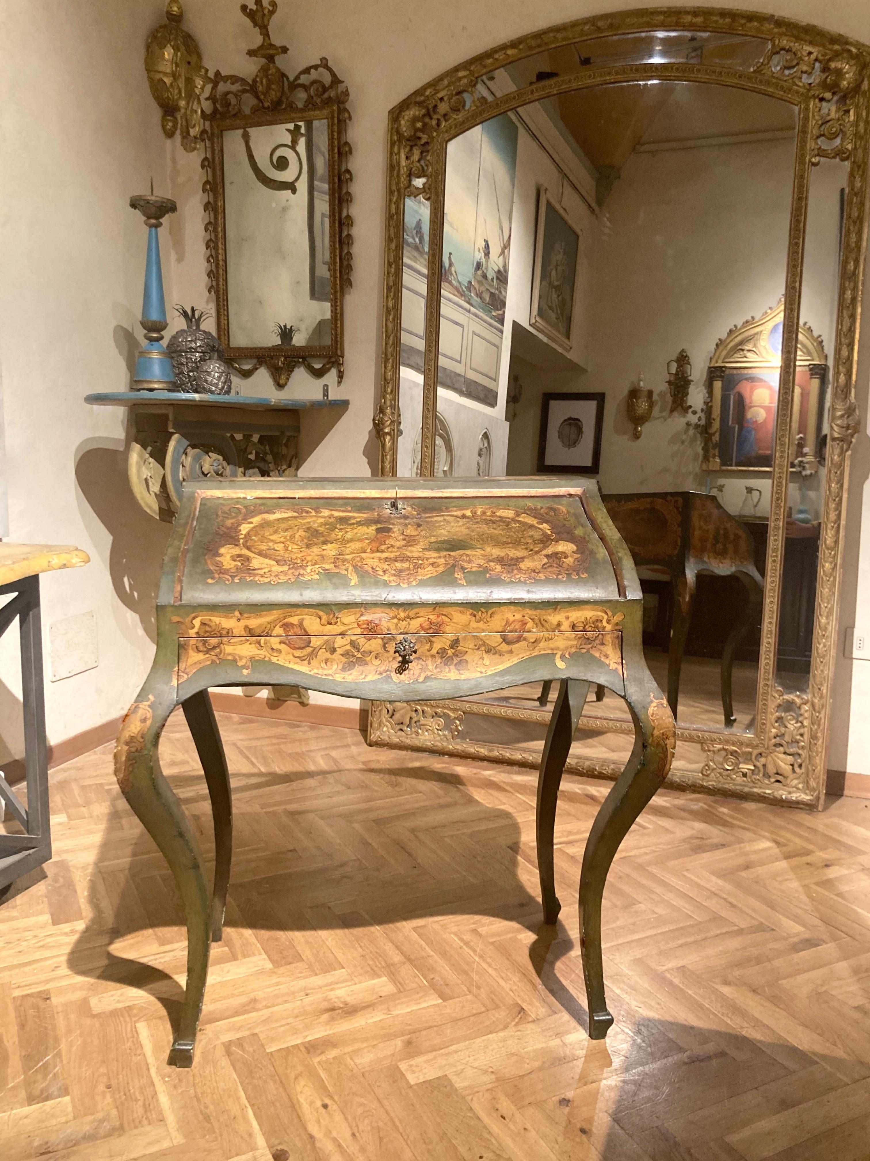 This lovely petite Italian Louis XV style slant-top writing desk is entirely decorated with hand painted lacquer featuring genre scenes, floral paintings and putto so fashionable during the Venetian rococo period. The writing table - wonderfully