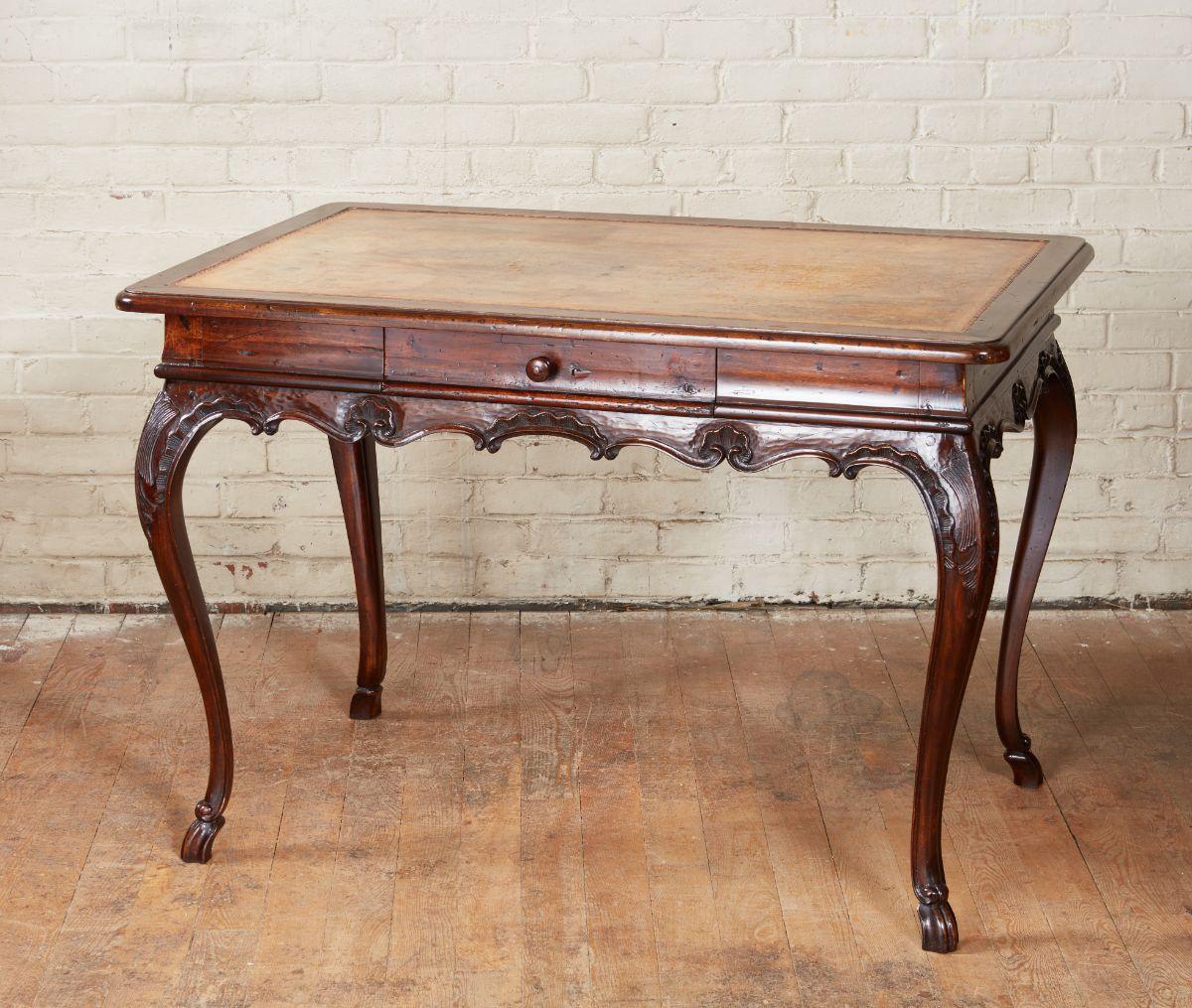 Fine Italian walnut rococo writing table, the lovely faded olive inset leather top with gilt tooled edge and thumb molded walnut banding over molded frieze with single drawer, the apron with scalloped and rocaille and shell carving and standing on