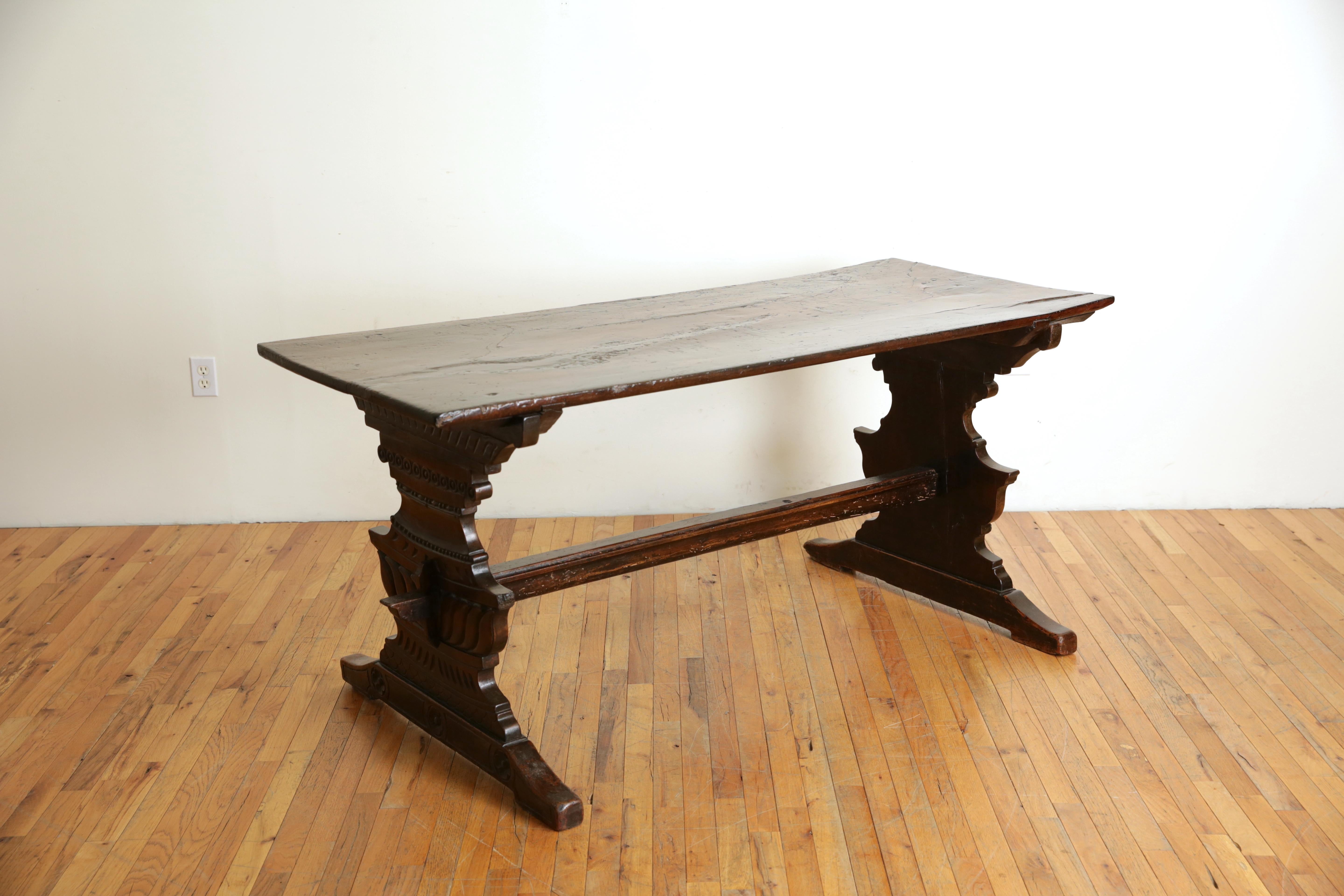 Having a thick one board rectangular top above a pair of trestle form supports beautifully carved in urn shapes with a number of decorative details and rosettes, the feet widely splayed, the supports joined by a thick stretcher, all elements