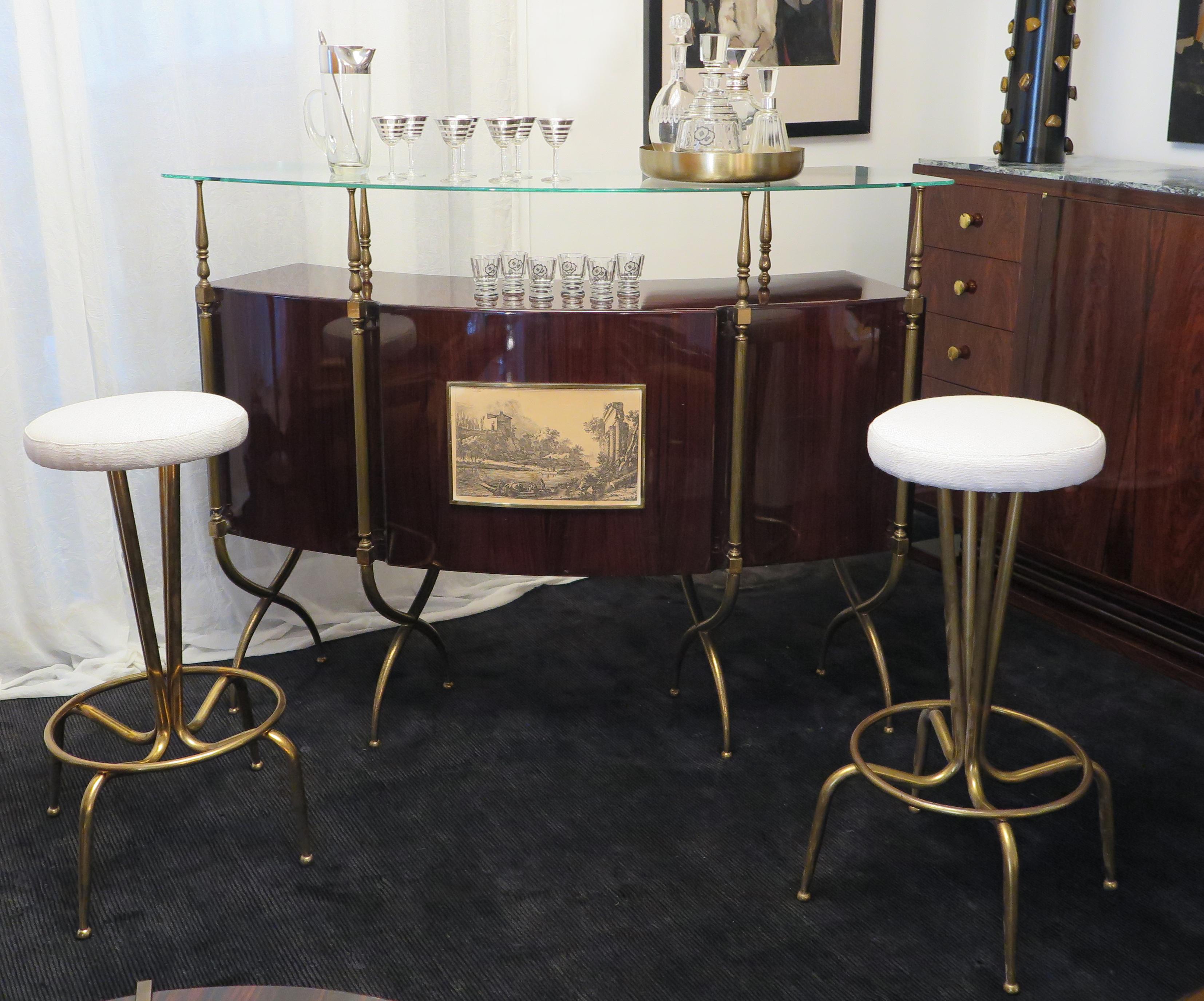 This unique curved Italian Mid-Century bar is crafted in Rosewood with a gloss finish in the style of Gio Ponti.  Stylized brass elements hold up glass top and run down the facade turning into the legs of the piece. The glass top adds lightness and