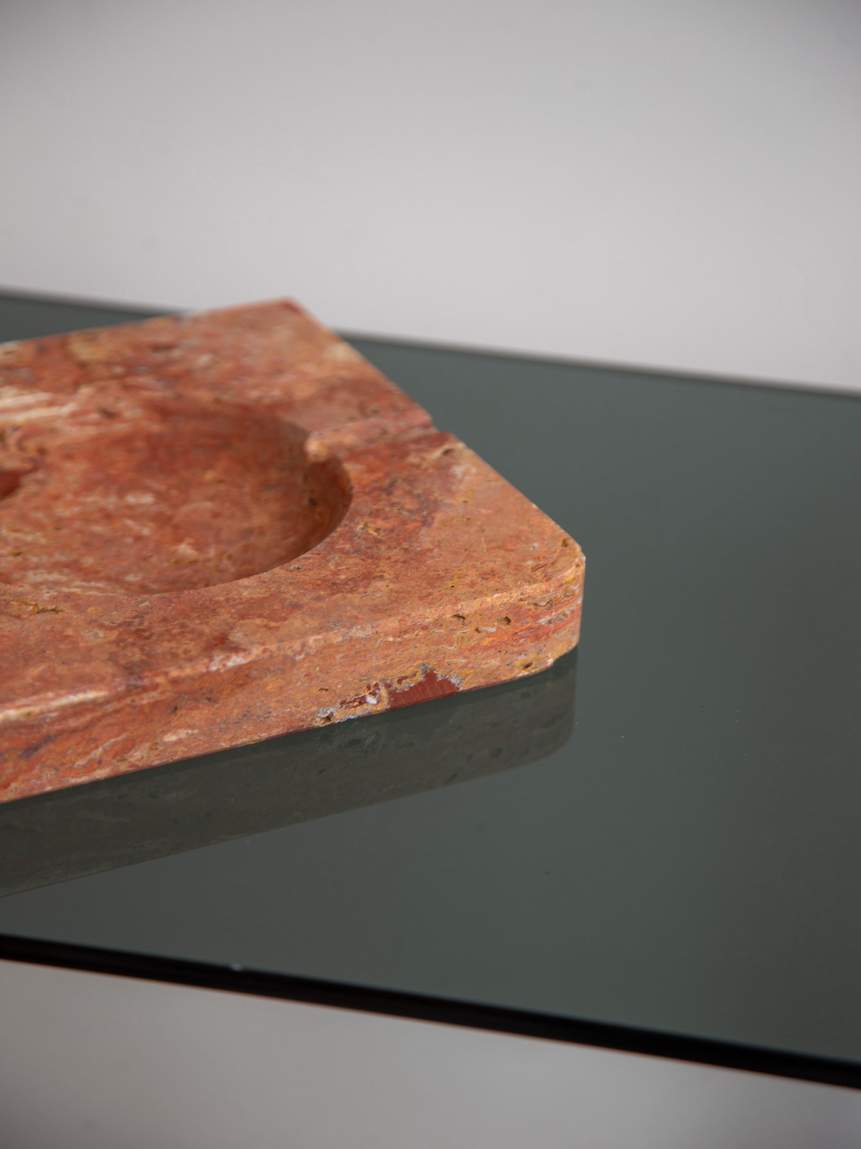 Cendrier raffiné en marbre massif Rosso Verona, fabriqué en Italie dans les années 1970. Le design carré minimaliste est rehaussé par un bol circulaire et une encoche subtile, créant un jeu sculptural de géométrie et de profondeur. Riche en tons