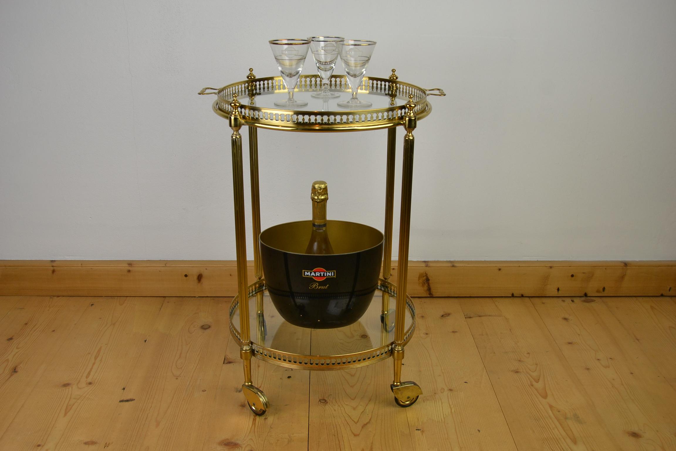 Stylish vintage round brass Italian bar cart - serving trolley from the 1950s.
It is marked with a label, made in Italy.
This two-tier drink trolley has two original clear glass shelves, the upper one is also a removable serving tray with handles