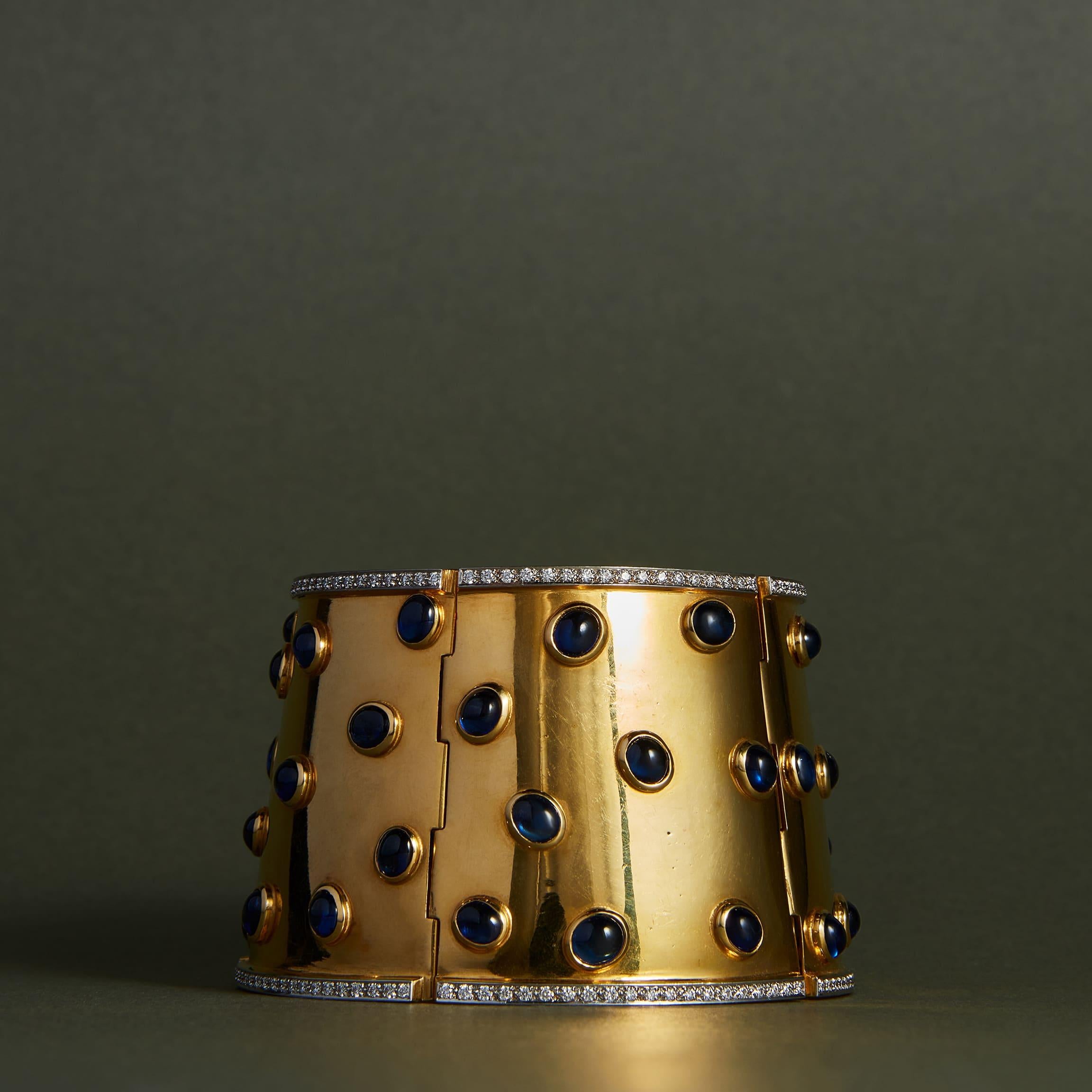 The ultimate statement jewel. This wide-hinged cuff bracelet of polished 18k yellow gold and platinum is set with cabochon sapphires, within edges embellished with lines of brilliant-cut diamonds.
Wide cuff bracelets are empowering jewels - sensual
