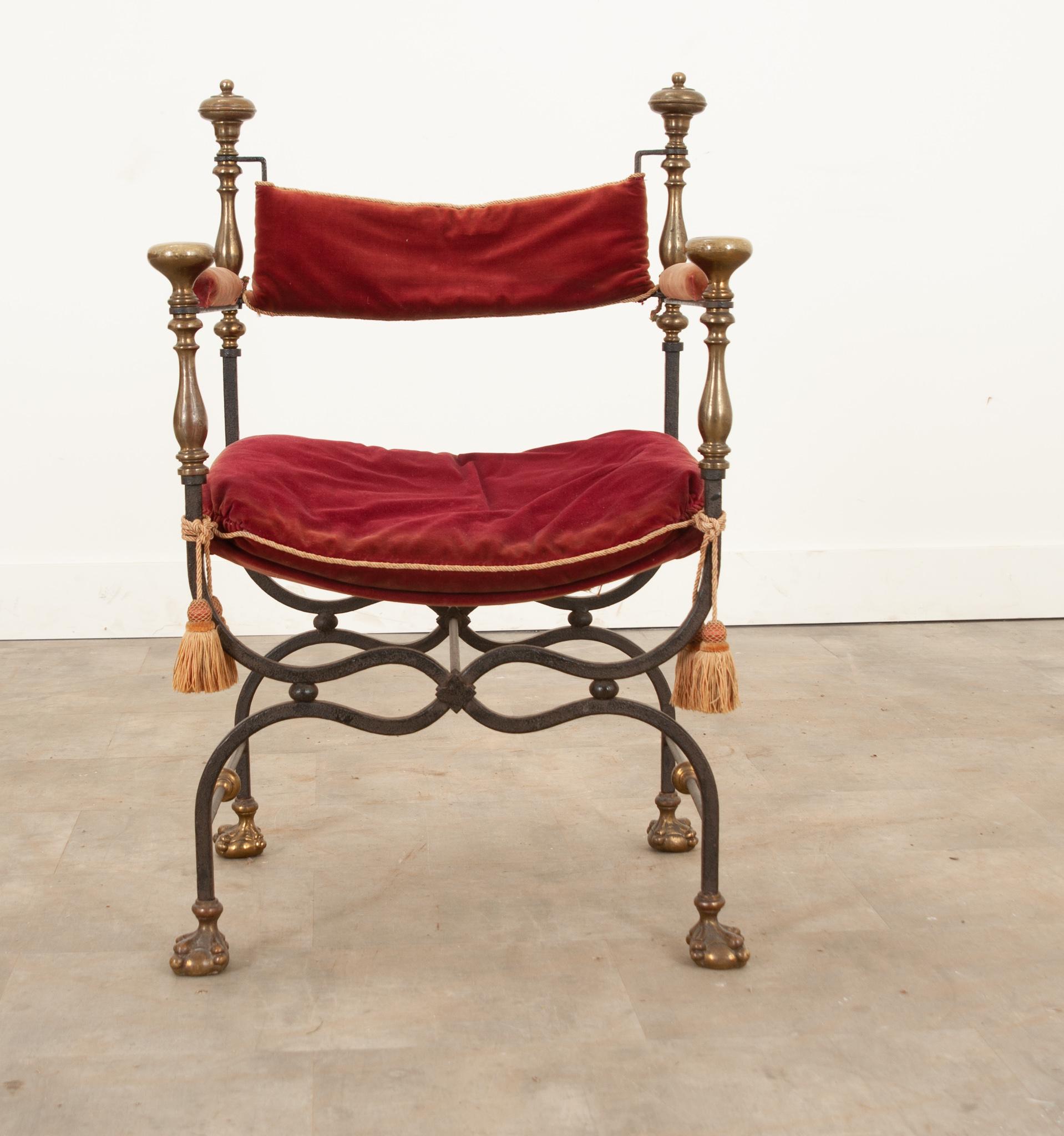 Une fabuleuse chaise Savonarola avec des coussins en velours rouge parfaitement usés et des attaches à pompons de qualité. Les embouts décoratifs en laiton contrastent magnifiquement avec les cadres en fer forgé à la main. Le coussin du bas et de