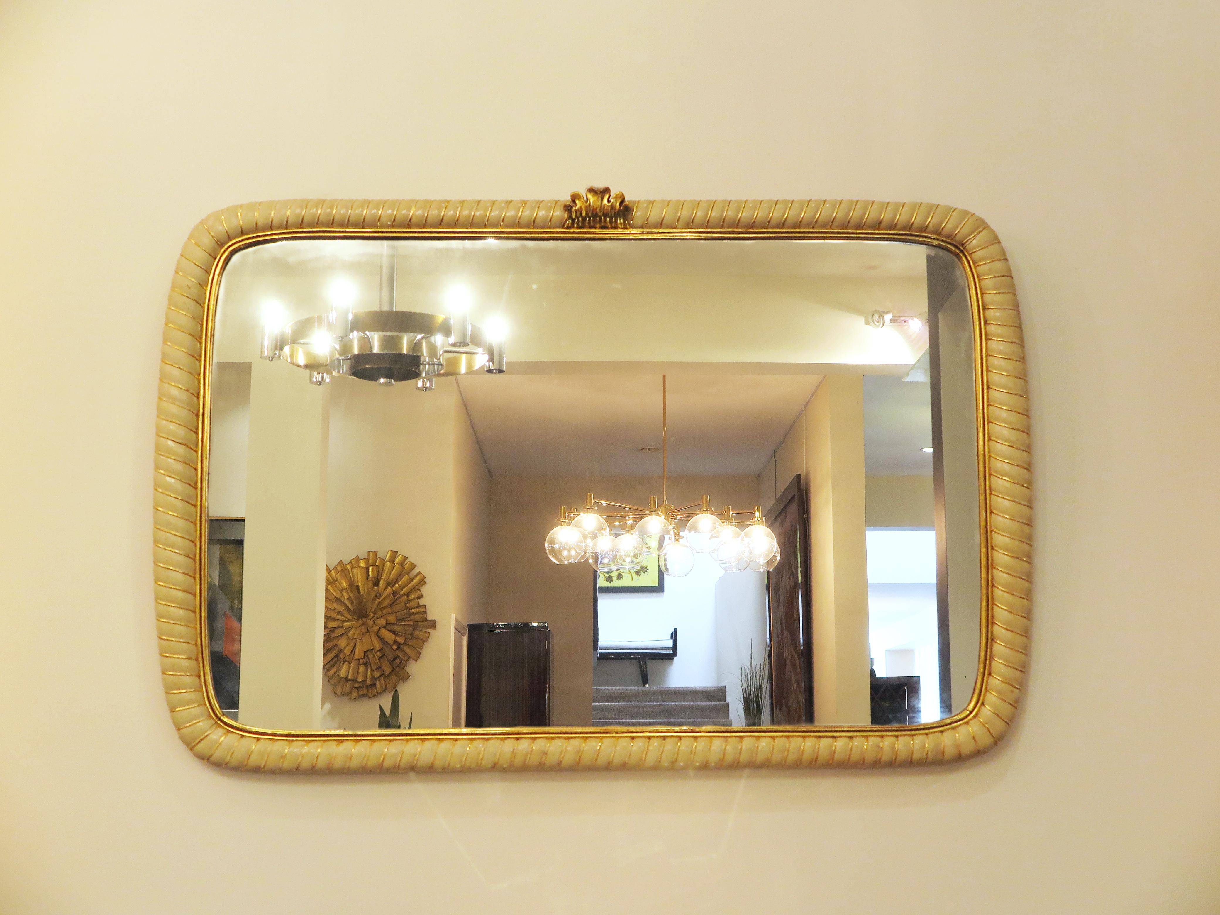 Italian mid-century mirror in ivory lacquer. The scalloped carved design features gilded divisions and a gilded crown-like ornamentation on the top. Original condition.