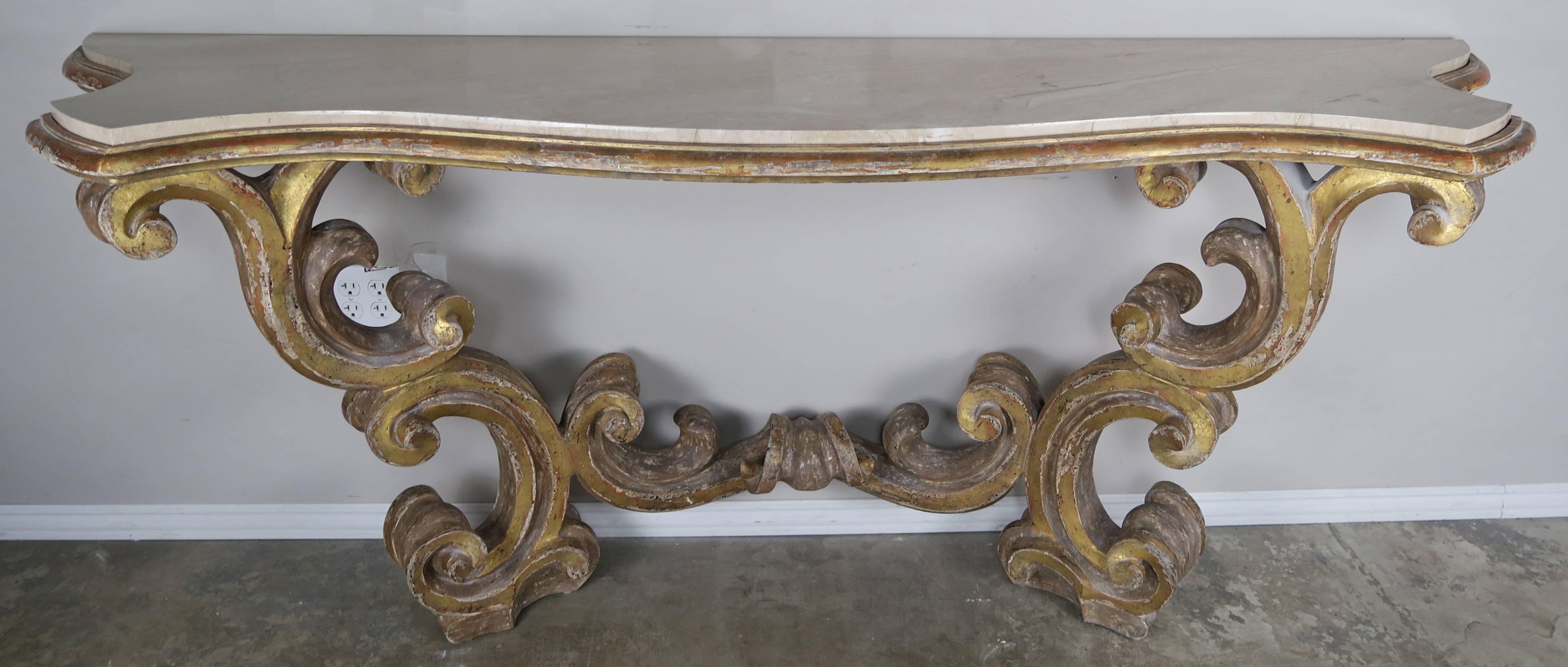 Italian scrolled giltwood carved console with an inset cream colored marble top. The table stands on two beautifully scroll shaped legs connected by a center stretcher.
 