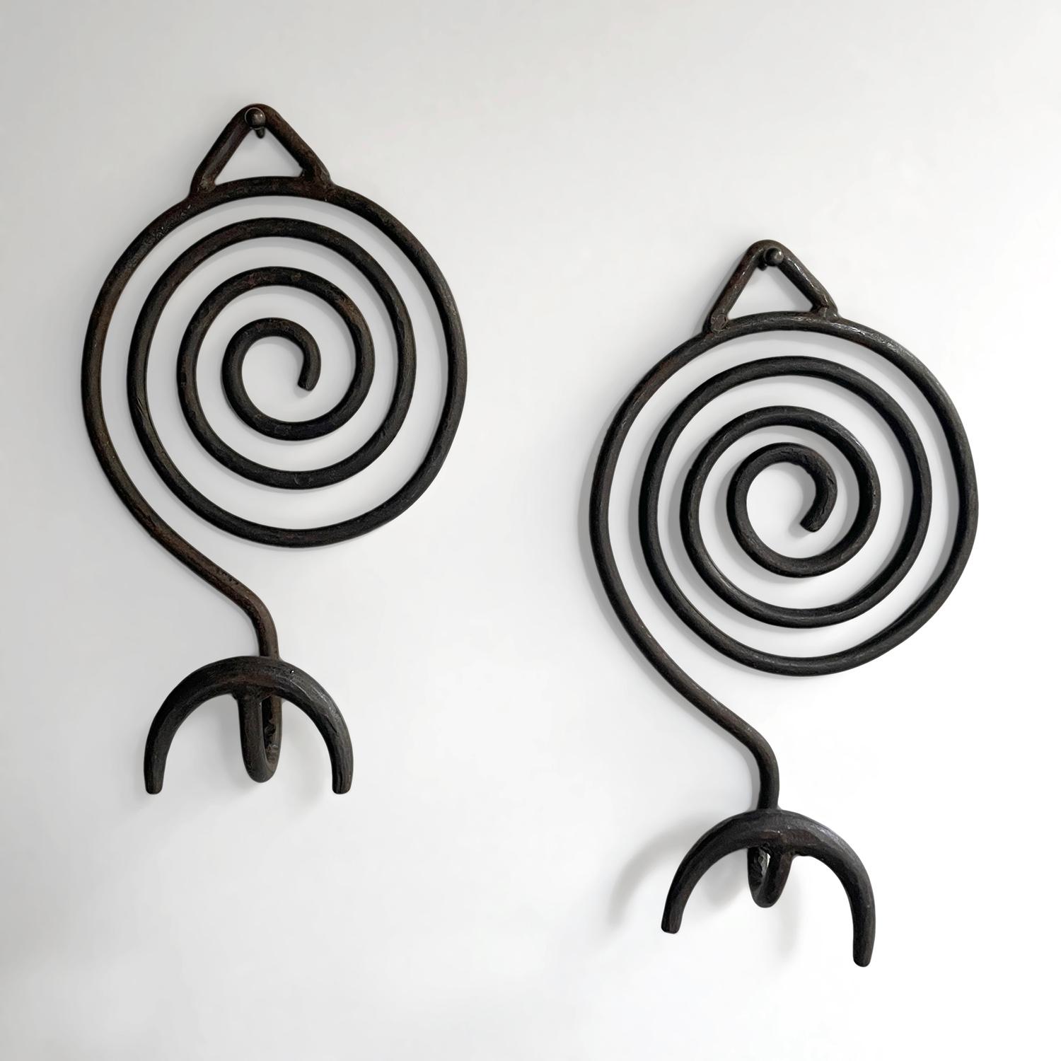 Pair of Italian sculpted Iron wall coat hooks 
Italy, circa 1960s 
These beautifully sculpted wall hooks are a dramatic statement piece
Whimsical spiraled back piece supports an arched lower hook
Both wall hooks have a single mounting loop 
Each