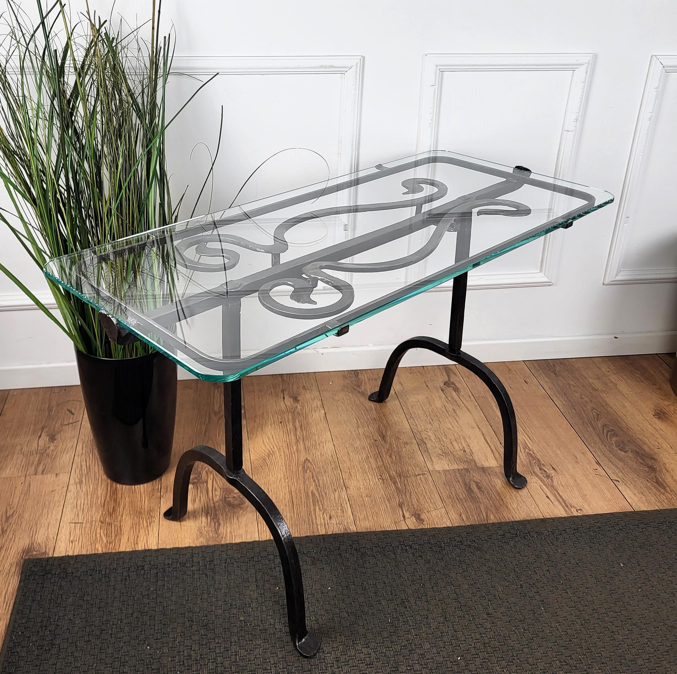Beautifully hand crafted wrought iron side table with strong and thick glass top, placed on a decorative frame. The legs, greatly shaped and forged with the typical finish of hand forging, are finished with round feet and centrally united with