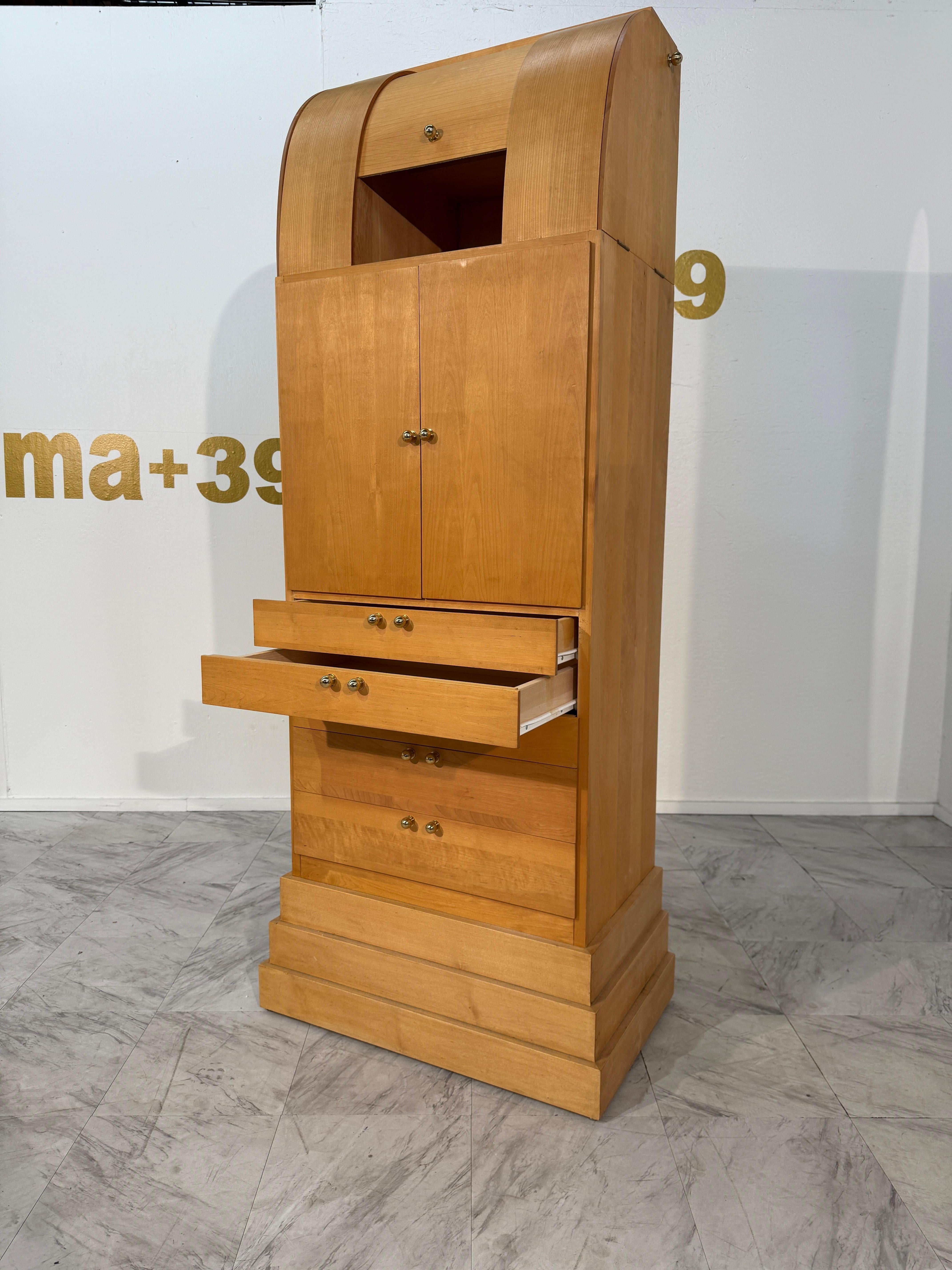 This tall Italian cabinet features an architectural silhouette, crafted from warm honey-toned wood with a gently curved top reminiscent of a vaulted ceiling. A stepped plinth base gives the piece a strong, grounded presence, echoing classical