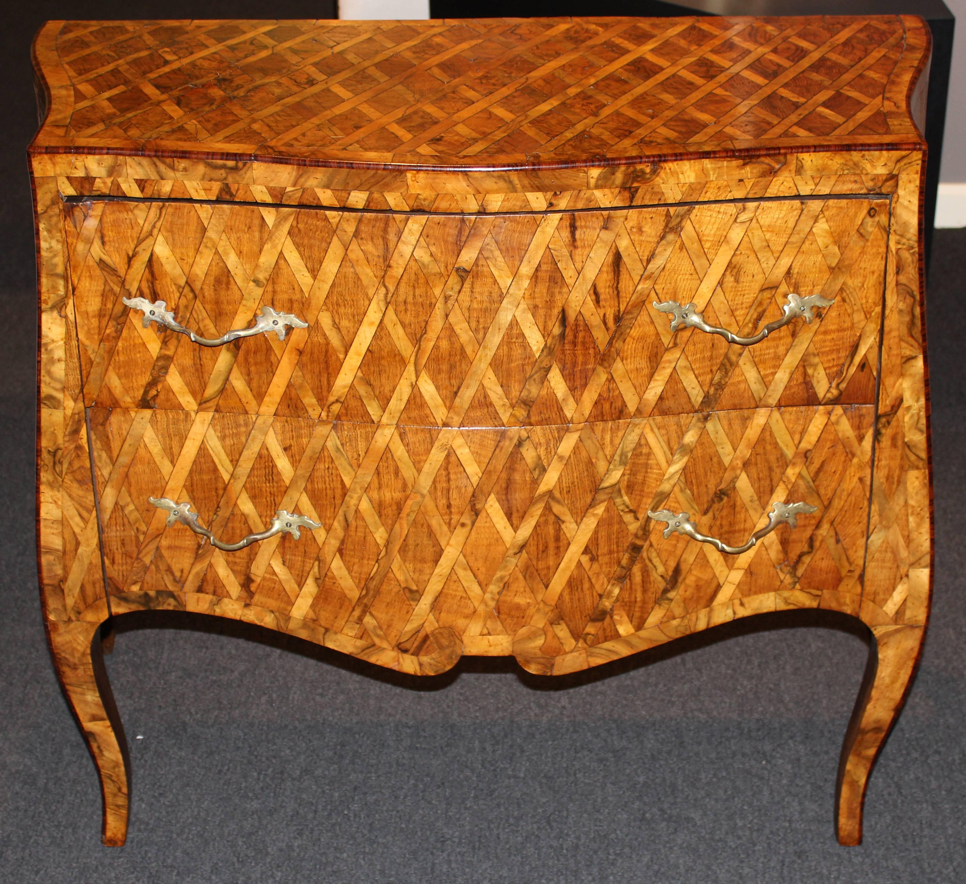 An exceptional Italian two-drawer fruitwood commode in serpentine form with conforming cross hatch and banded parquetry top with molded edges surmounting two long drawers with original brass pulls and continuing cross hatch parquetry and banded
