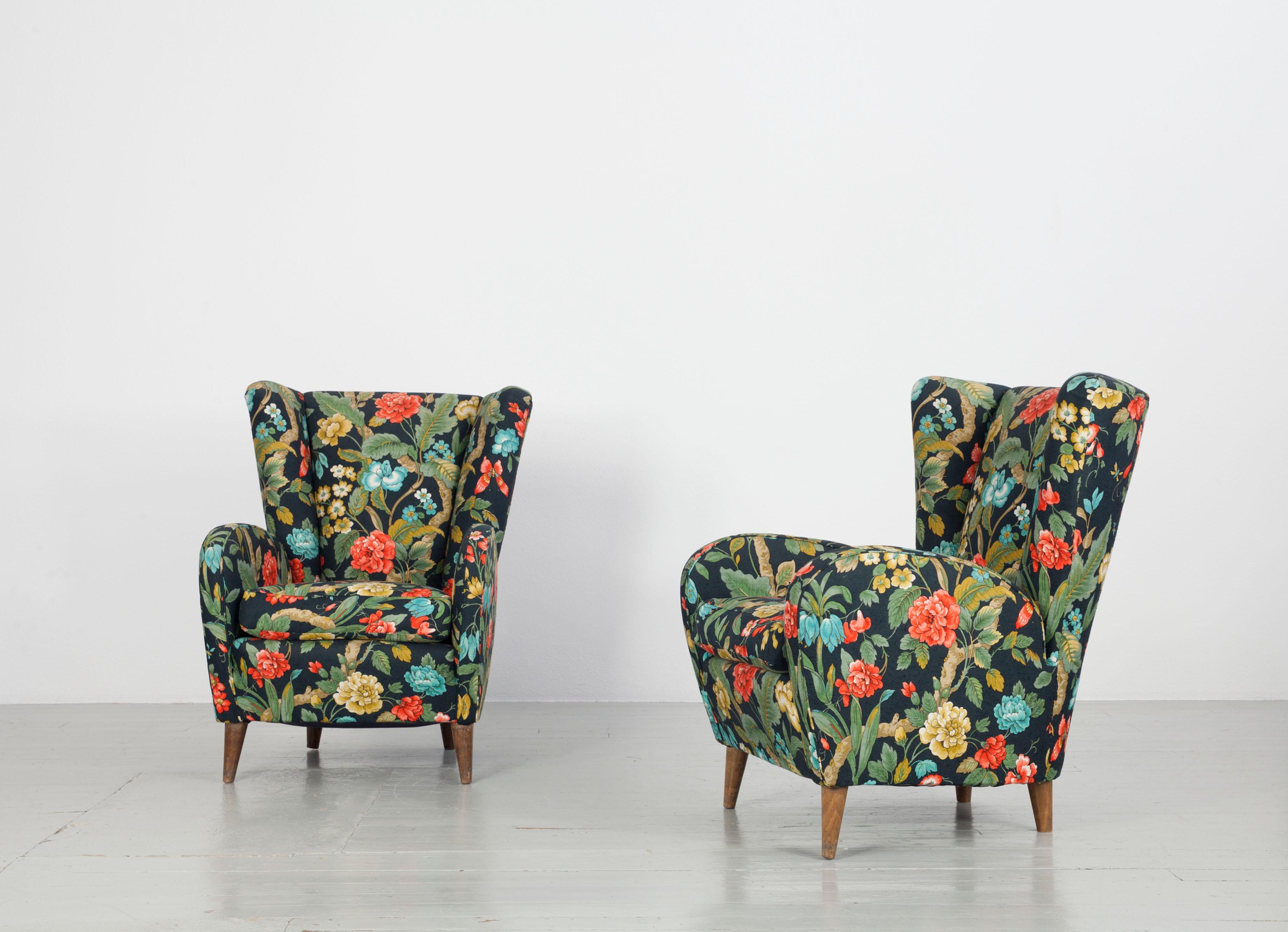 This Italian pair of armchairs in the style of Paolo Buffa was made in the 1950s. The particularly comfortable pieces of furniture catch the eye with their colourful floral fabric cover. The upholstery and the shape of the wing chairs support the