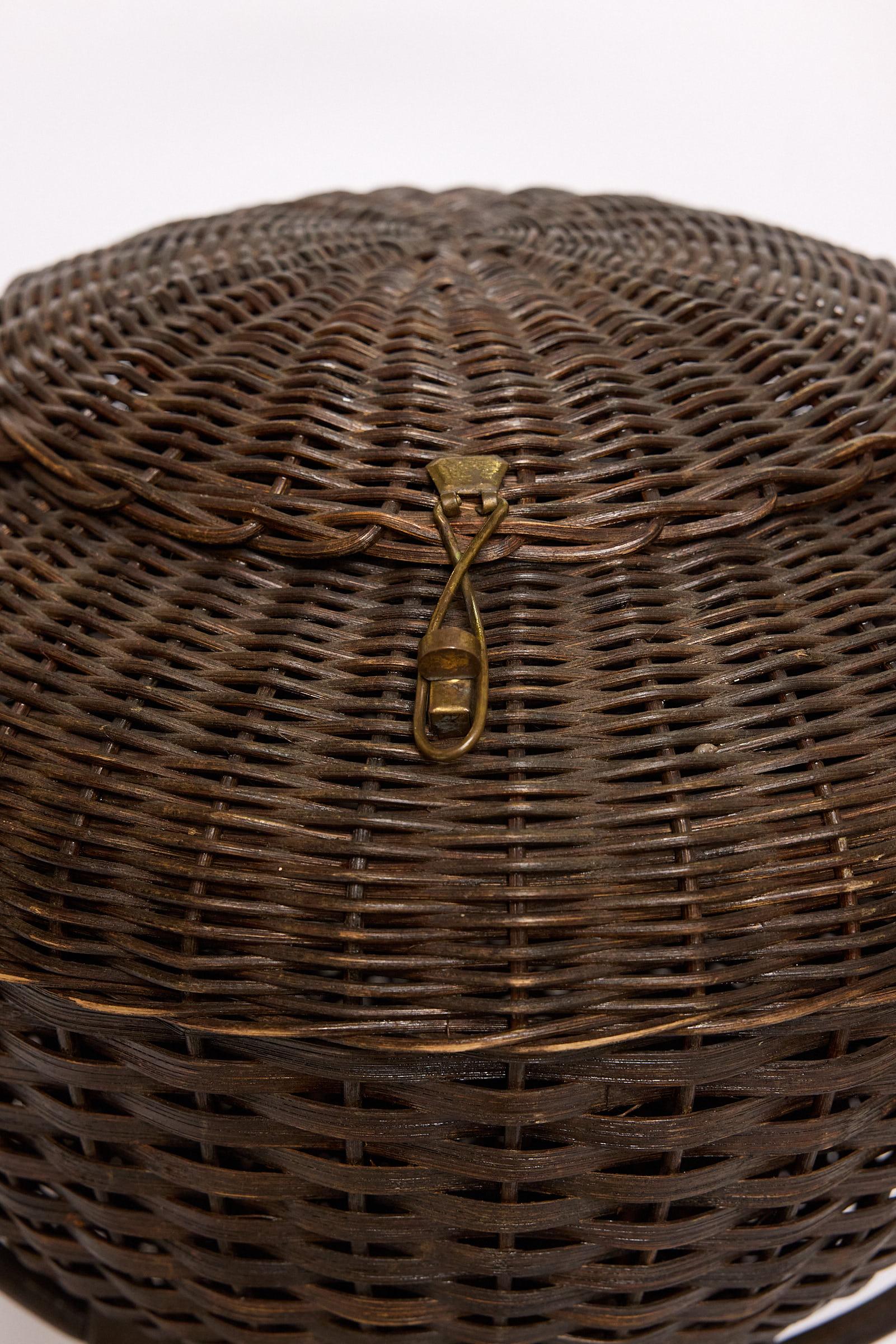 Cestino in vimini italiano dei primi del Novecento a forma di piattino con coperchio incernierato in pelle e ottone che si apre su una cavità utilizzata storicamente per il materiale da cucito. Il cestino poggia su una base a piattaforma che si