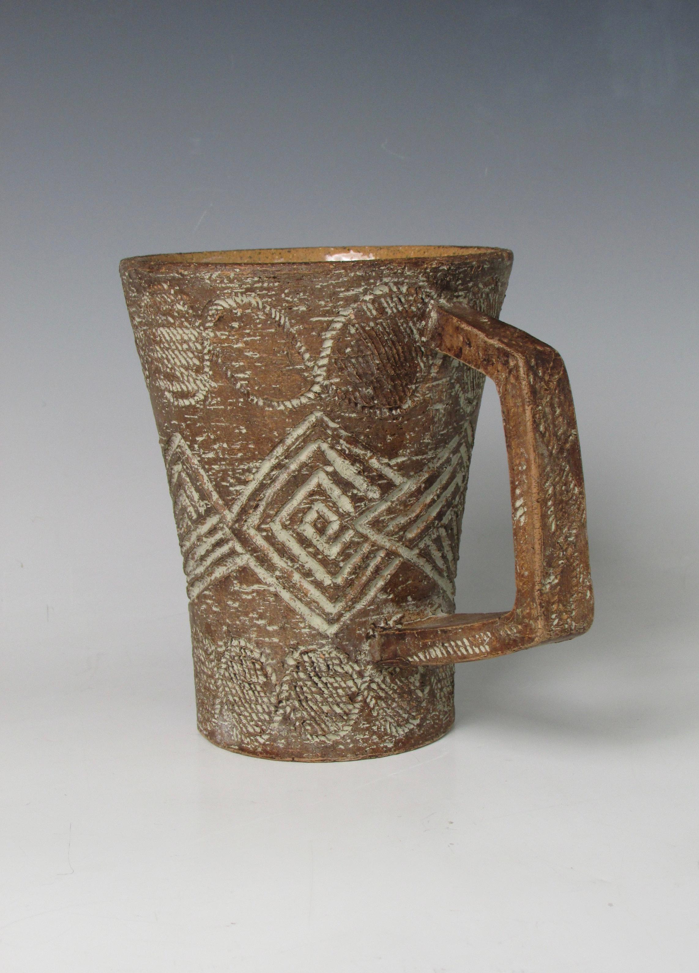 An Italian sgraffito redware pottery pitcher with an angular handle. 
The cork or bark like textural surface has a varied tawny, coffee and cork coloration. The incised surface features cement gray highlighting within the design. The interior is