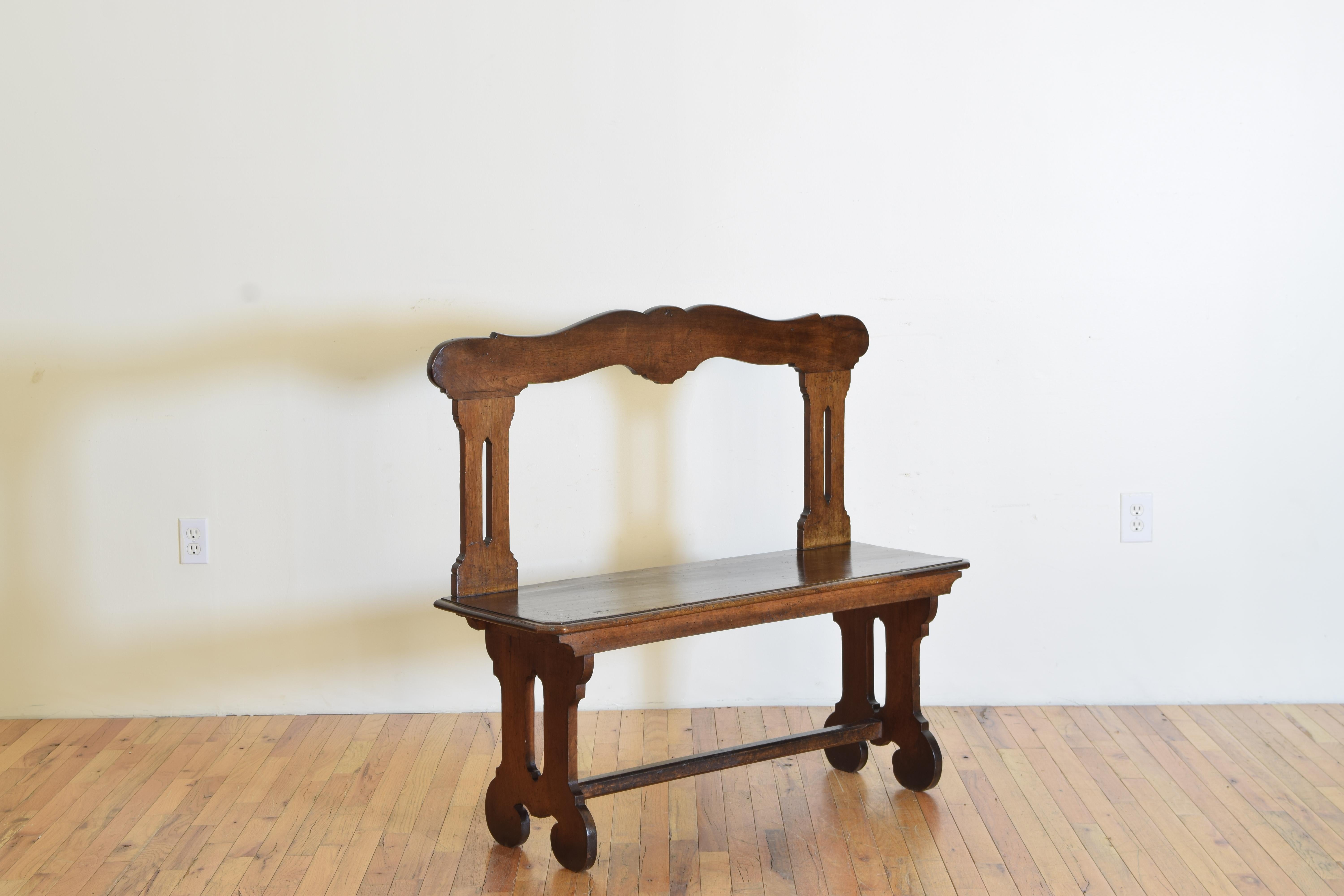 This mid 19th Century small hall bench or church pew with a rectangular seat raised on lyre-shaped legs joined by a stretcher and has a backrest that is hand-carved, pierced, and shaped.