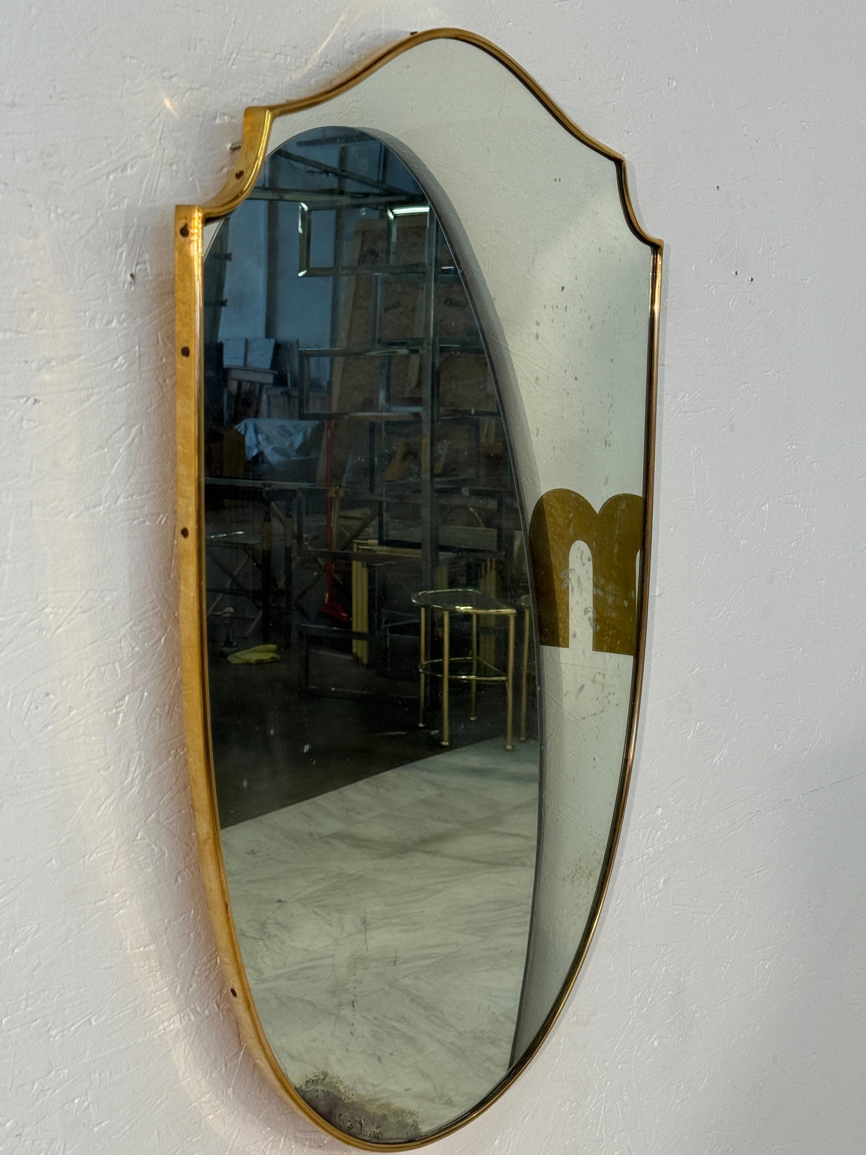 A classic Italian wall mirror in an elegant shield shape, framed with a slender brass border. Its gently curved silhouette and warm metallic edging give it both sophistication and timeless appeal. The mirror reflects mid-century Italian design