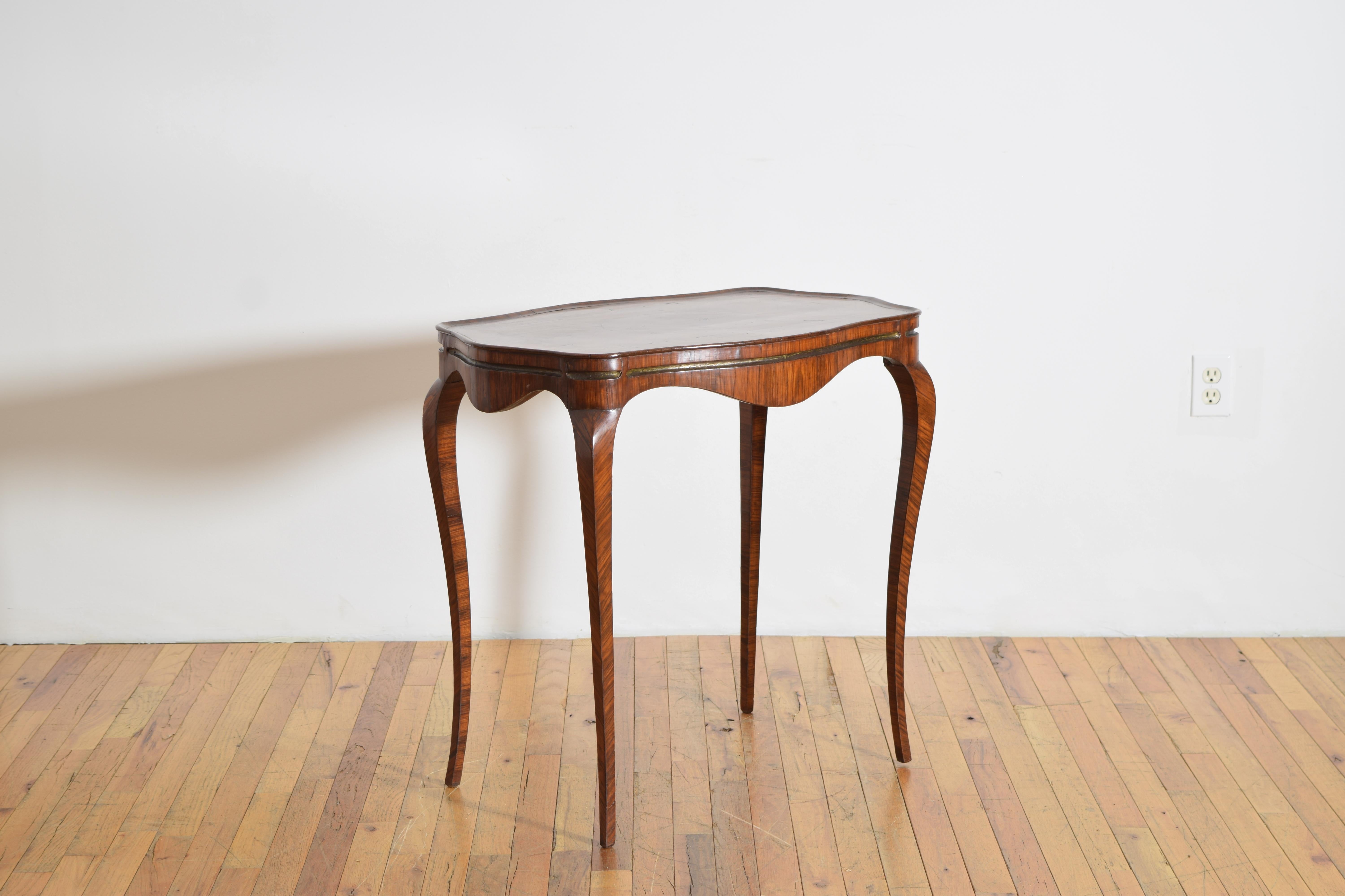 Le plateau est de forme serpentine avec un épais bord galbé plaqué en bois de rose avec un motif rectangulaire centré sur un ovale, le tablier façonné avec une grande incrustation de laiton sur tous les côtés, reposant sur des pieds cabriole effilés.