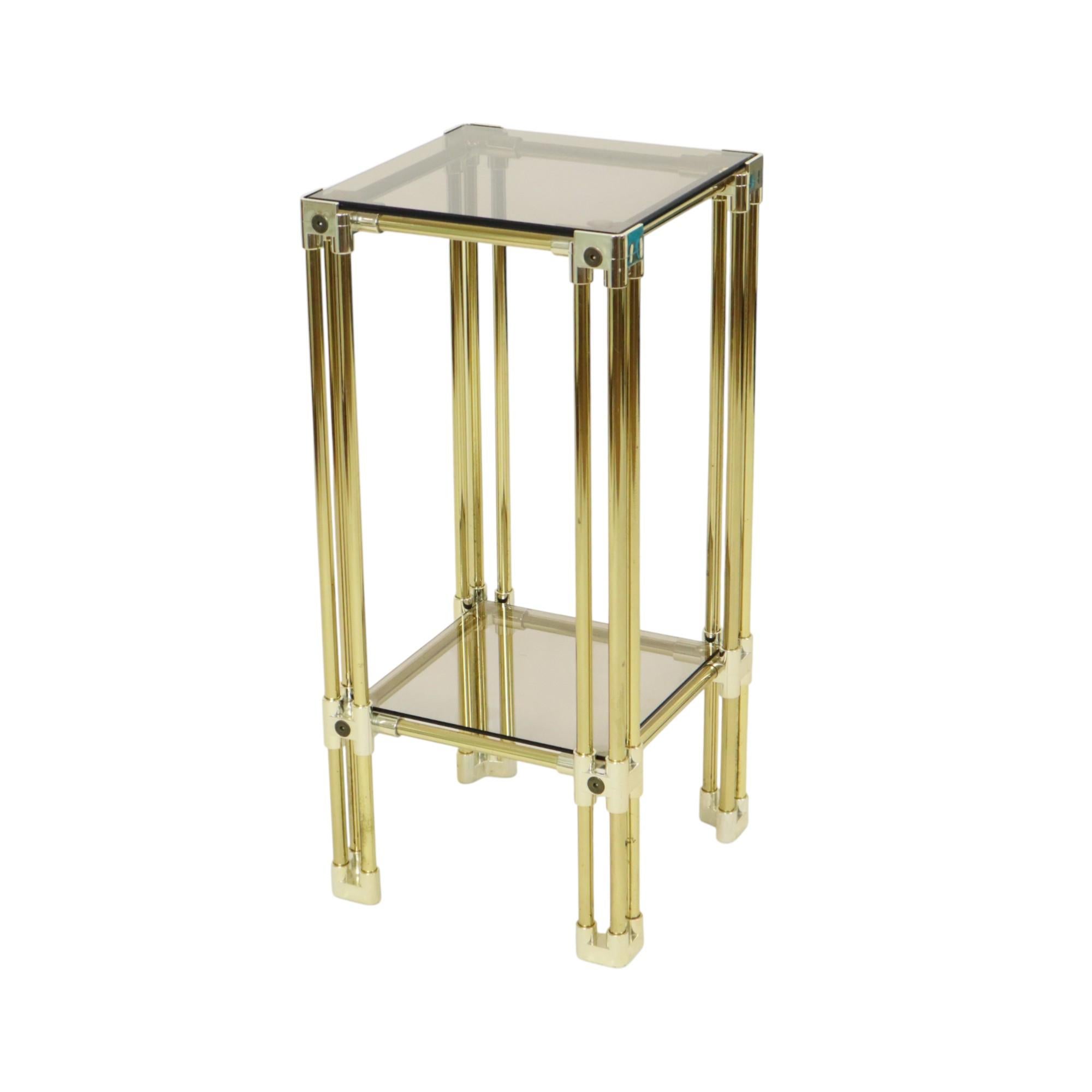 Tavolino/portavaso dal design vintage in metallo cromato e plastica color oro, con due ripiani in vetro fumé, interamente in stile Hollywood Regency, Italia, anni Settanta.

Questo piccolo e pratico tavolino è dotato di due ripiani in vetro che sono