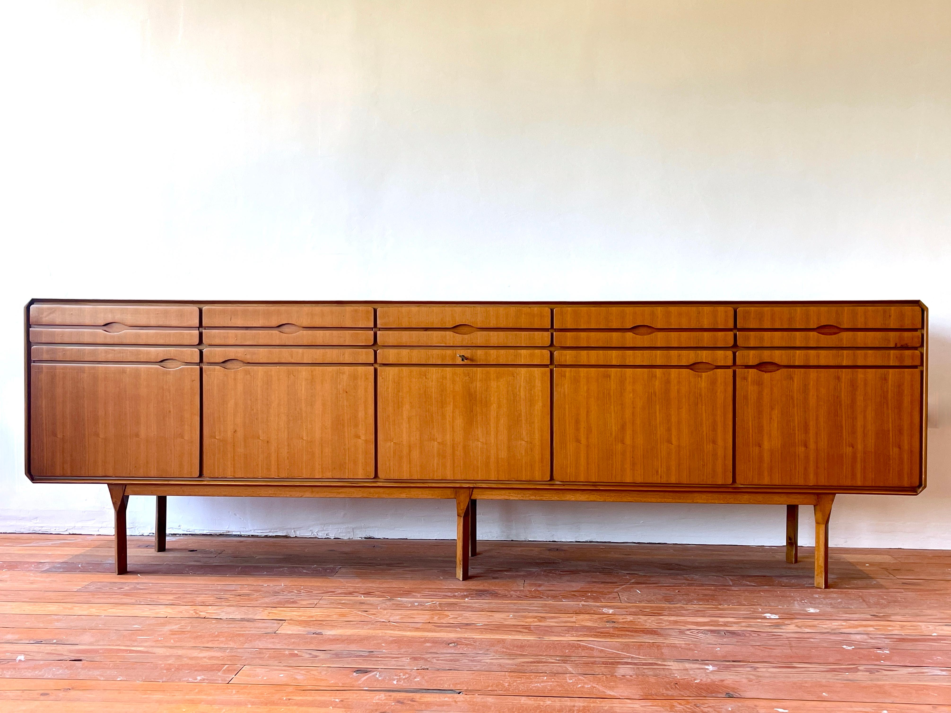 incredible Italian sideboard produced by La Permanente Mobili Cantù circa 1950's. 

Massive teak wood with recessed carved horizontal lines, curved sides and ornate legs. 

White inlay on top veneer - with 5 drawers and 5 doors with open