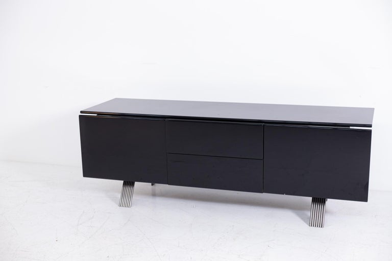 Beautiful and modern 1970s sideboard of Italian manufacture. The sideboard is made of glossy black lacquered wood. It is divided into three sections, the two single side doors have a storage compartment inside, while the center are two drawers. The
