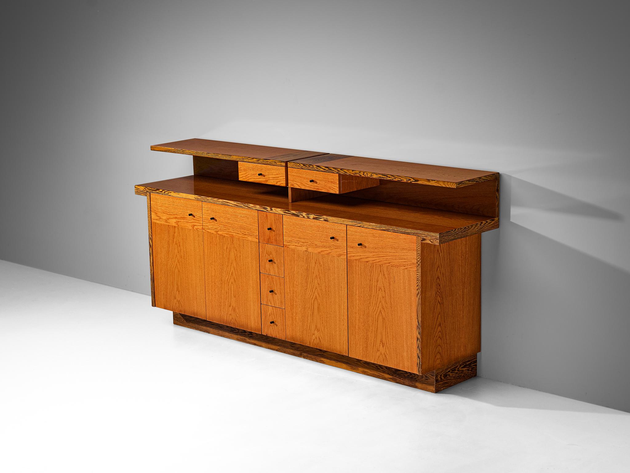 Sideboard, wengé veneer, ash veneer, Italy, 1970s.

This exquisite credenza exemplifies the aesthetic sensibilities that prevailed during the 1970s. The front facade features a captivating interplay of geometric shapes arranged in a symmetrical