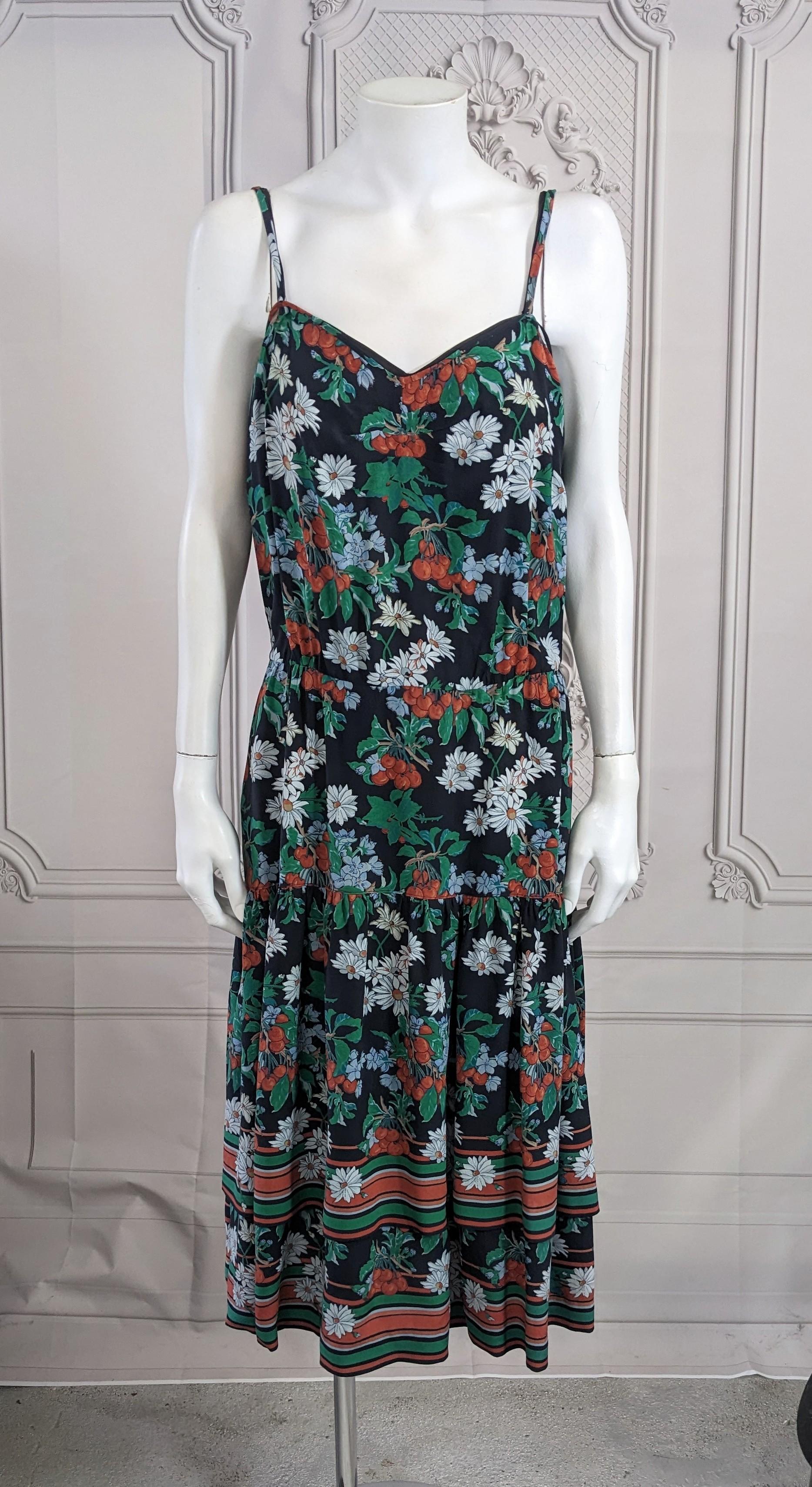 Charming Italian Silk Crepe Print Ruffle Dress from the 1980's. Floral and fruit print on black ground with double full ruffle on skirt with striped edge. Comes with matching black slip. 
Grosgrain interior waist band with back button and zip
