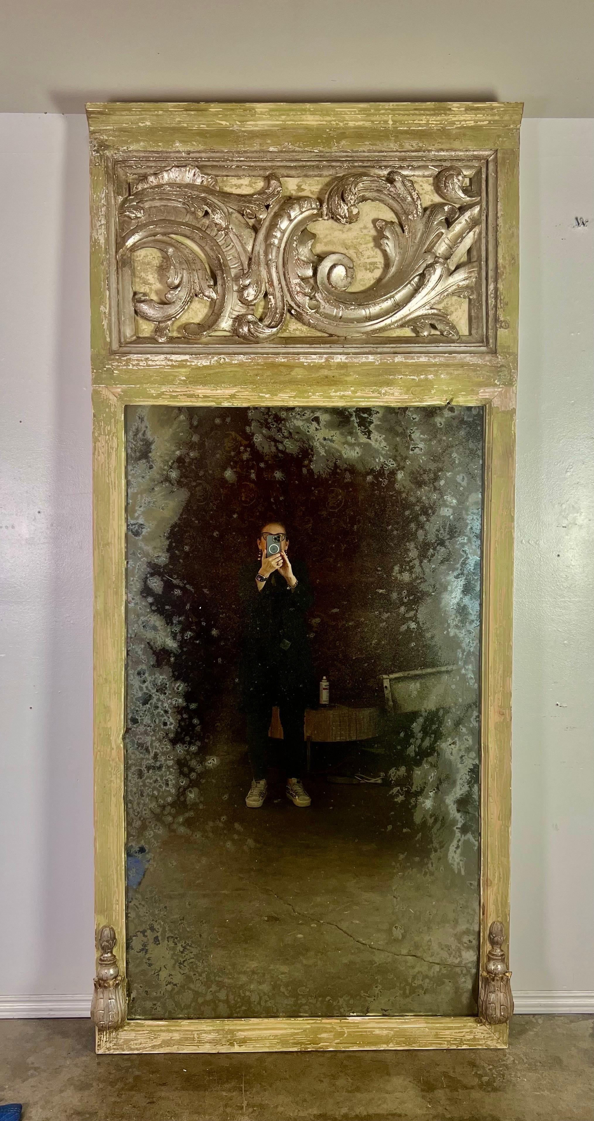 A silver gilt and painted mirror crafted from 19th--century carved wood architectural pieces, adorned with swirling scrolls and acanthus leaves, creates a visually captivating piece.  The addition of antiqued smoky mirror inset adds a touch of