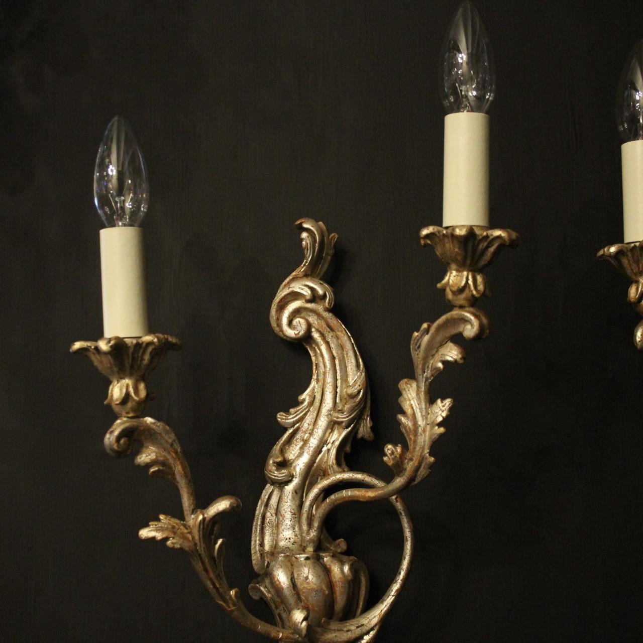 A decorative Italian carved silver giltwood and toleware twin arm antique opposing wall lights, the foliated toleware leaf scrolling arms with wooden leaf bobeche drip pans, issuing from an ornate opposing Acanthus leaf silvered wooden scrolling