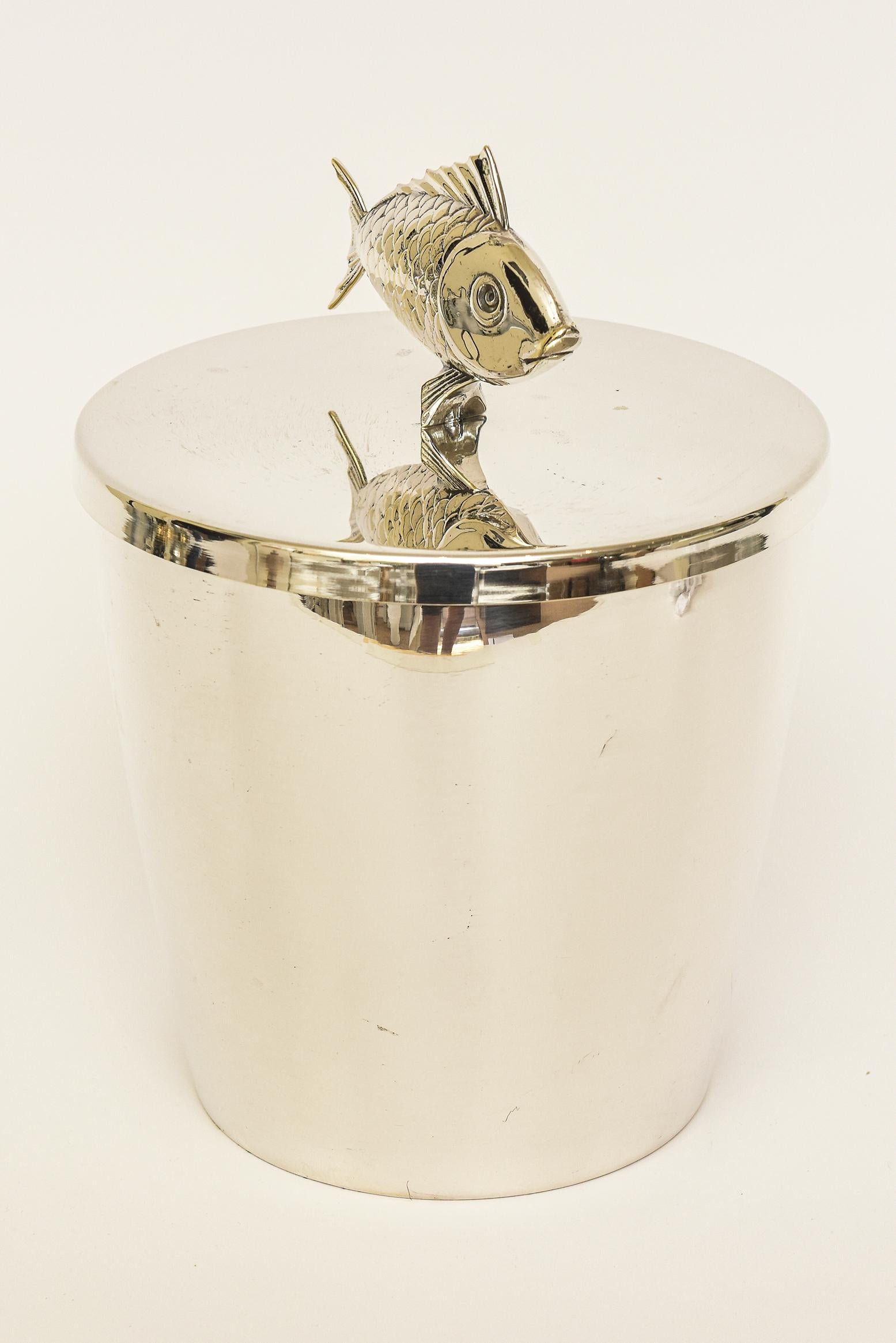 This delightful and fun Italian vintage polished silver-plate ice bucket has a wonderful fish motif as the top handle.
It is from the 70's. Says silverwear on the bottom with cartouches of which we have not done the research on. It has a satin
