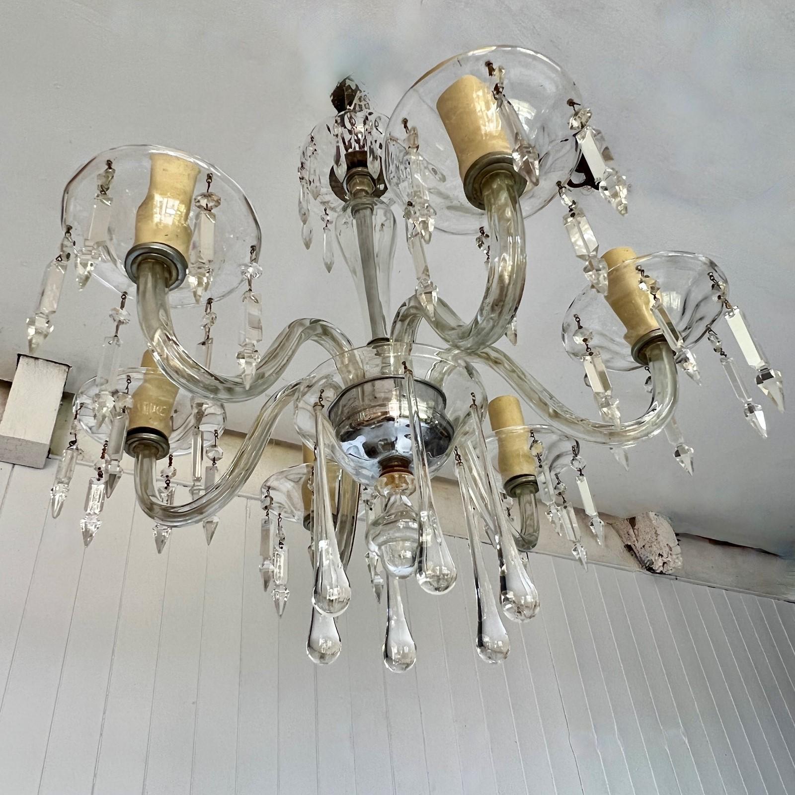 Un lampadario in cristallo italiano di grande eleganza. Questo lampadario con colonna centrale ovoidale in vetro è sormontato da una rosa circolare e da lustri. In basso si trova la grande coppa di vetro con il piatto d'argento a contrasto da cui