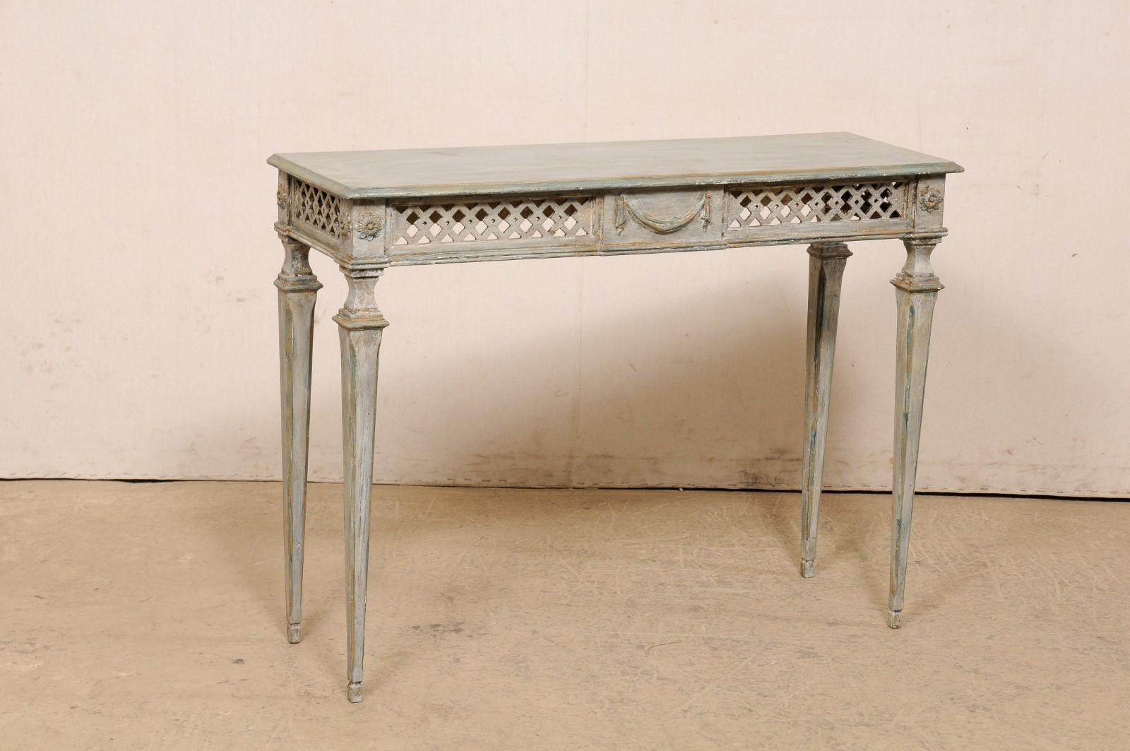 An Italian carved and painted wood console table from the Mid-20th Century. This vintage table from Italy has a slender, rectangular top over an apron with beautifully pierce-carved lattice about three sides, a swag carved embellished plaque at