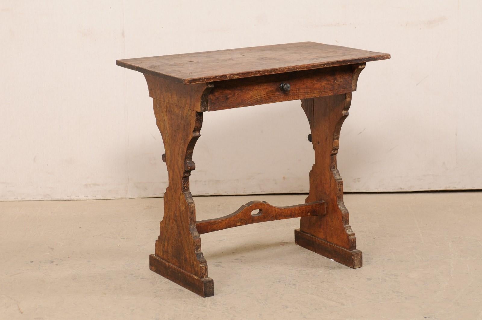 An Italian small sized table, or writing desk, from the 19th century. This antique table from Italy features a rectangular-shaped top overhanging an apron fitted with a single drawer at one long side. The table is raised on a pair of hour-glass