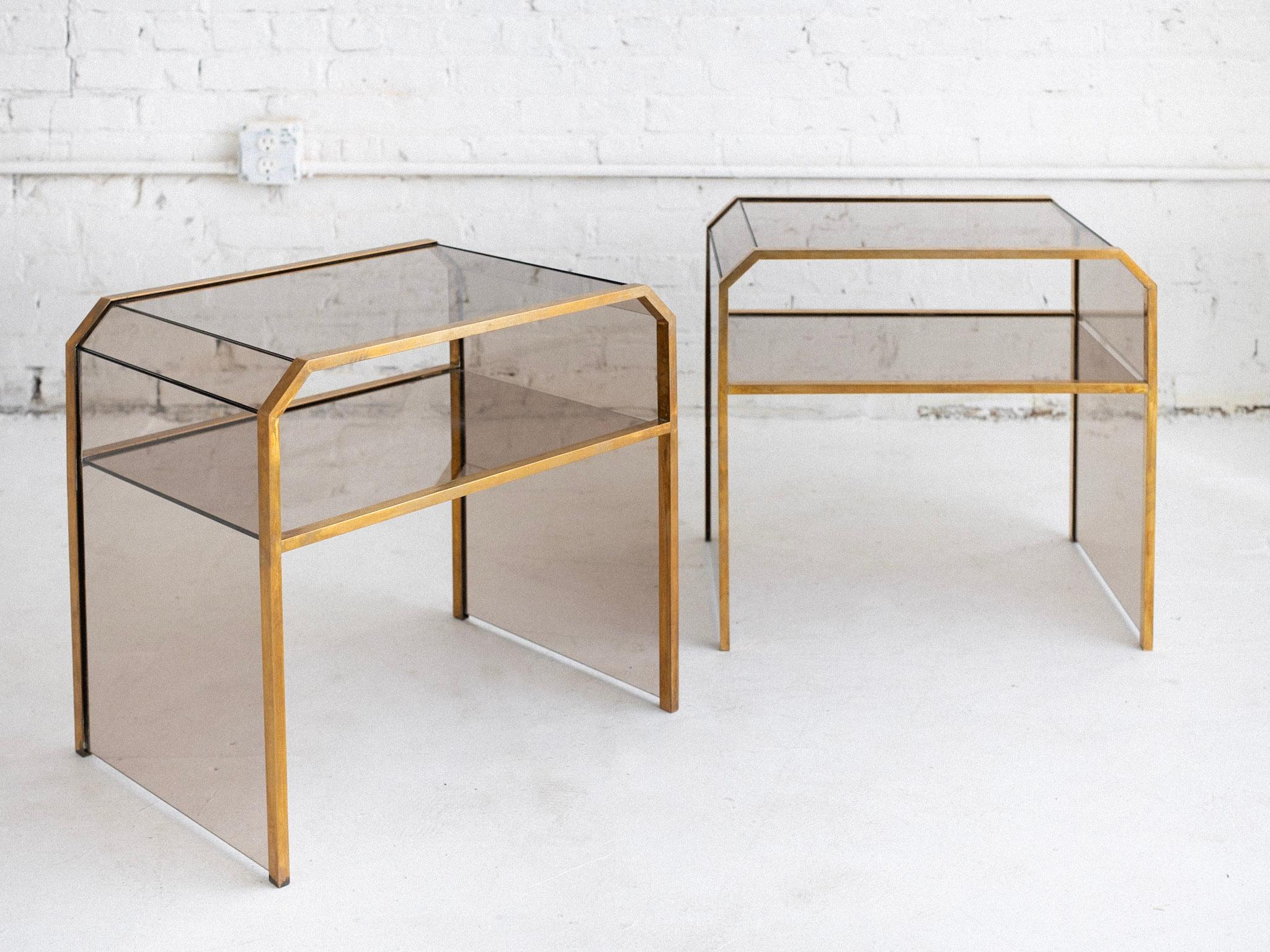 A pair of late mid century Italian glass and brass side tables. In the style of Max Ingrand’s, Fontana Arte or Gallotti & Radice. Warm smoke tone glass and patinaed brass frames. Geometric silhouette. Sold as a pair. Sourced in Northern Italy.