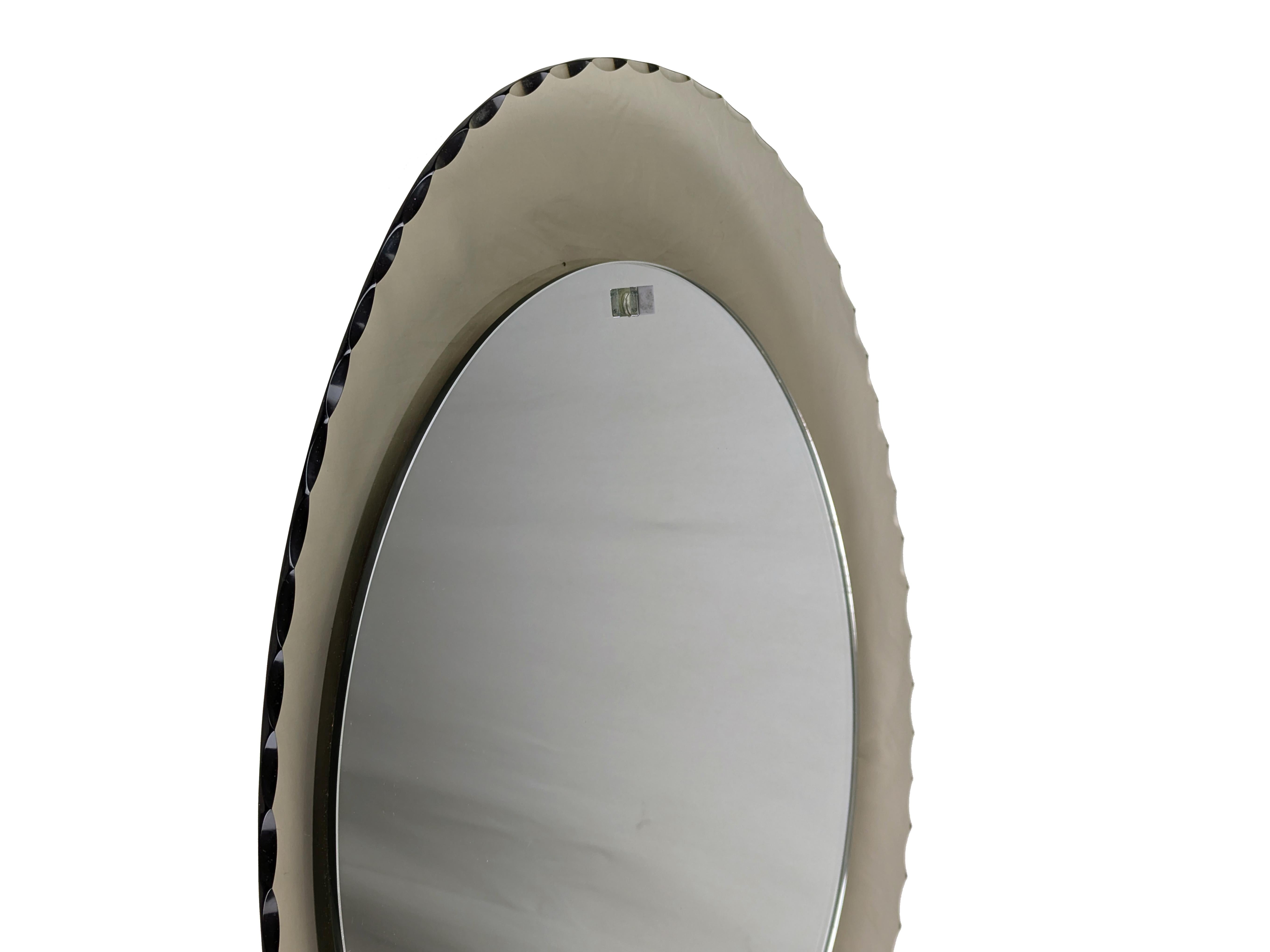 Bellissimo specchio da parete ovale con cornice convessa in vetro fumé. L'intero perimetro è decorato con un fitto lavoro di molatura. Il telaio è in ottime condizioni. La superficie a specchio presenta alcuni segni di ossidazione come mostrato