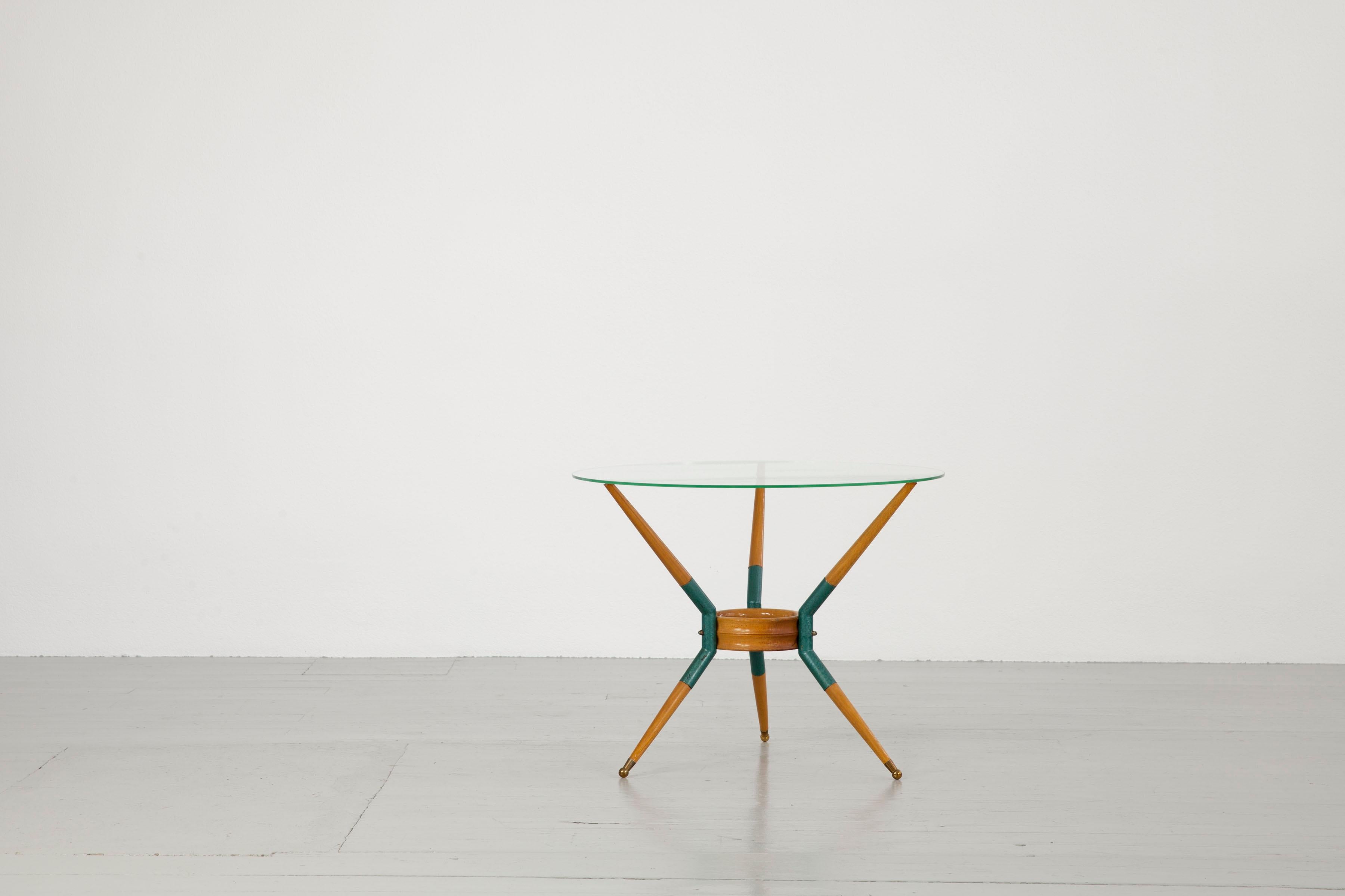 This elegant sofa table was made in Italy in the 1950s. The round glass top is supported by three, beautifully worked beech wood legs. The three legs are connected by a round wooden shelf and decorated with brass elements and brass finishes. Part of