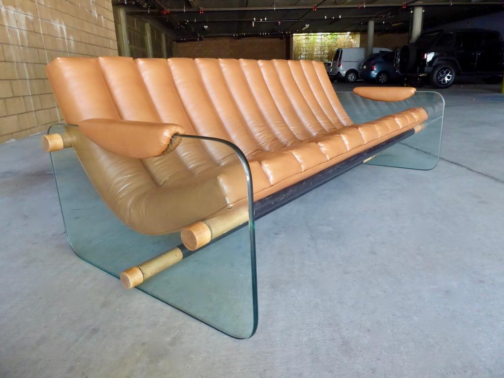 A glass-sided sofa with channeled leather upholstery attributed to Italian designer Fabio Lenci, circa 1969. The glass sides are secured with wood and enameled steel struts that end in circular walnut caps. The upholstered section is cradled and