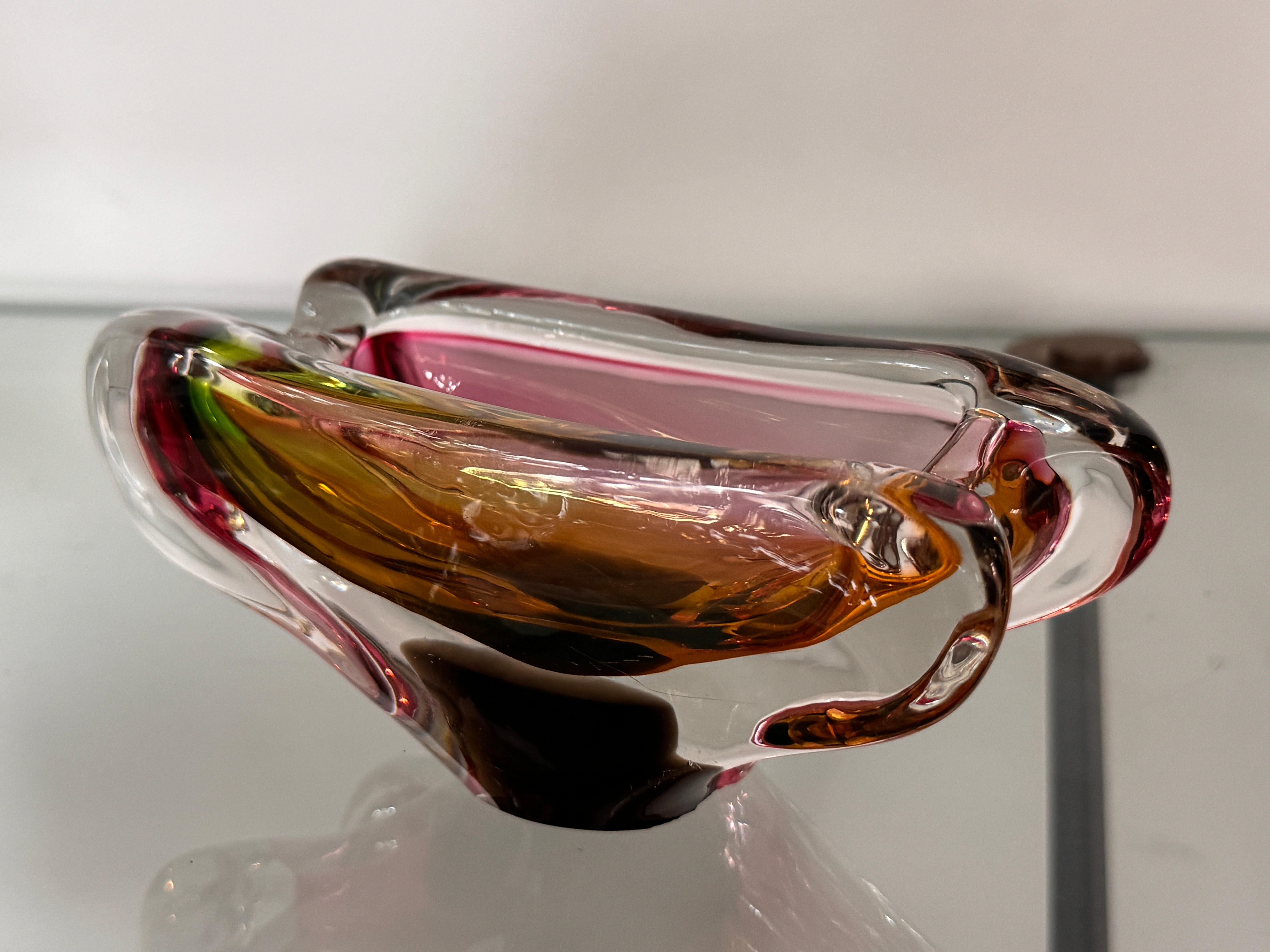 Remarquable cendrier en verre de Murano selon la technique sommerso, présentant des tons ambrés, roses et verts.
Sa forme organique avec deux encoches latérales le rend parfait comme cendrier à cigares, tout en servant de pièce décorative raffinée