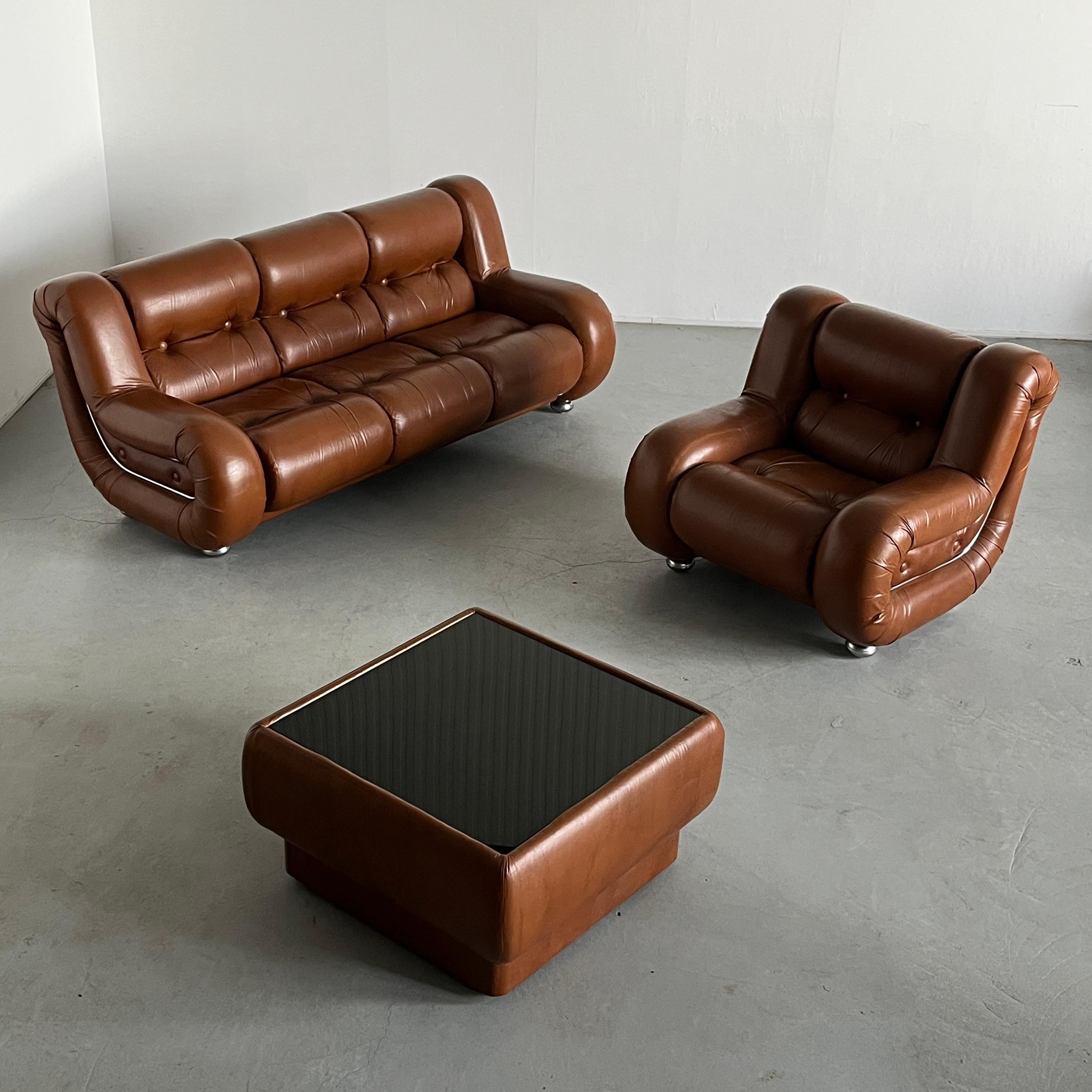Uno splendido set di sedute vintage italiano composto da un divano a tre posti, una poltrona e un tavolino in pelle color cognac. L'acciaio cromato a forma di goccia delinea i profili del divano e della poltrona, aggiungendo un tocco modernista.